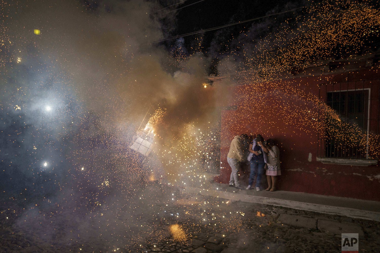  People cover themselves in front of a man wearing a "torito," a bull-shaped harness equipped with fireworks, during a Christmas celebration in Antigua, Guatemala, Dec. 25, 2021. (AP Photo/Moises Castillo) 