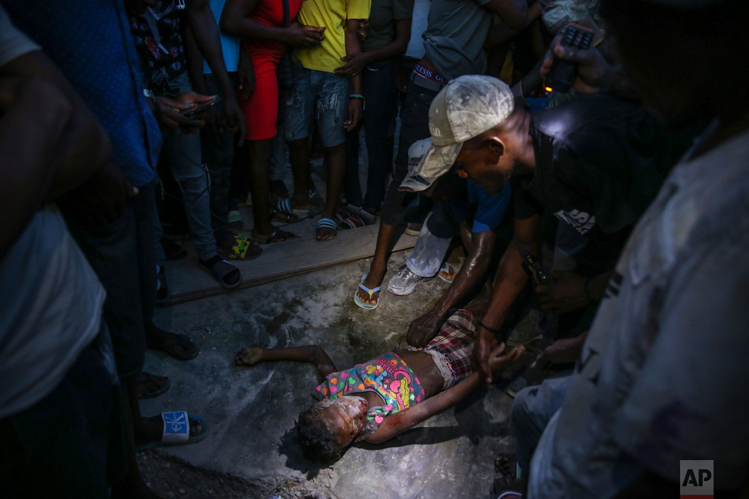  People look at the body of Esther Daniel, 7, who died under the rubble of a house destroyed by the earthquake in Les Cayes, Haiti, Saturday, Aug. 14, 2021. A 7.2 magnitude earthquake struck Haiti on Saturday, with the epicenter about 125 kilometers 