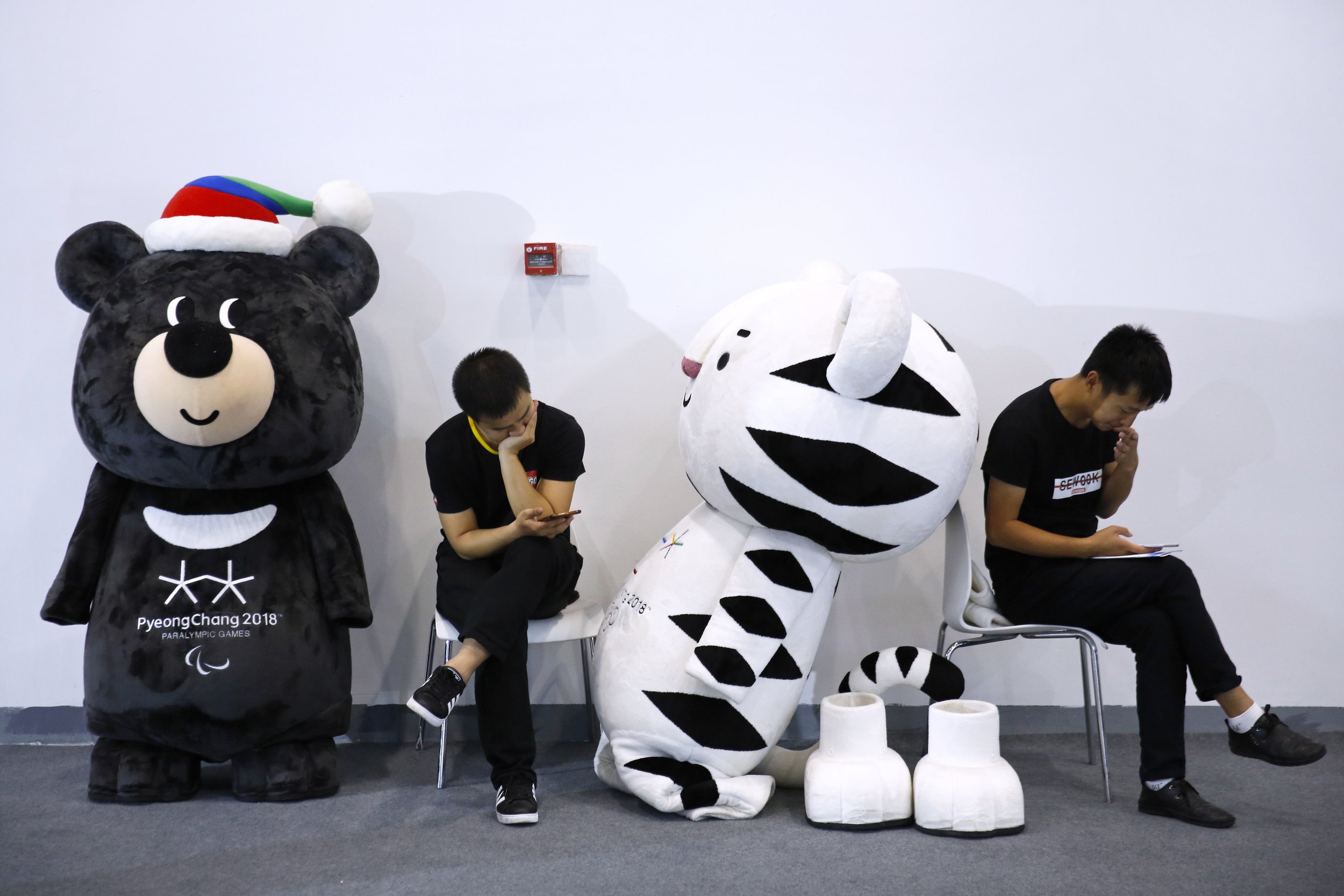  Workers browse their phones next to the mascots for the 2018 Pyeongchang Winter Olympics and Paralympic Games near the South Korean booth during the World Winter Sports Expo in Beijing, Sept. 7, 2017.  (AP Photo/Andy Wong) 