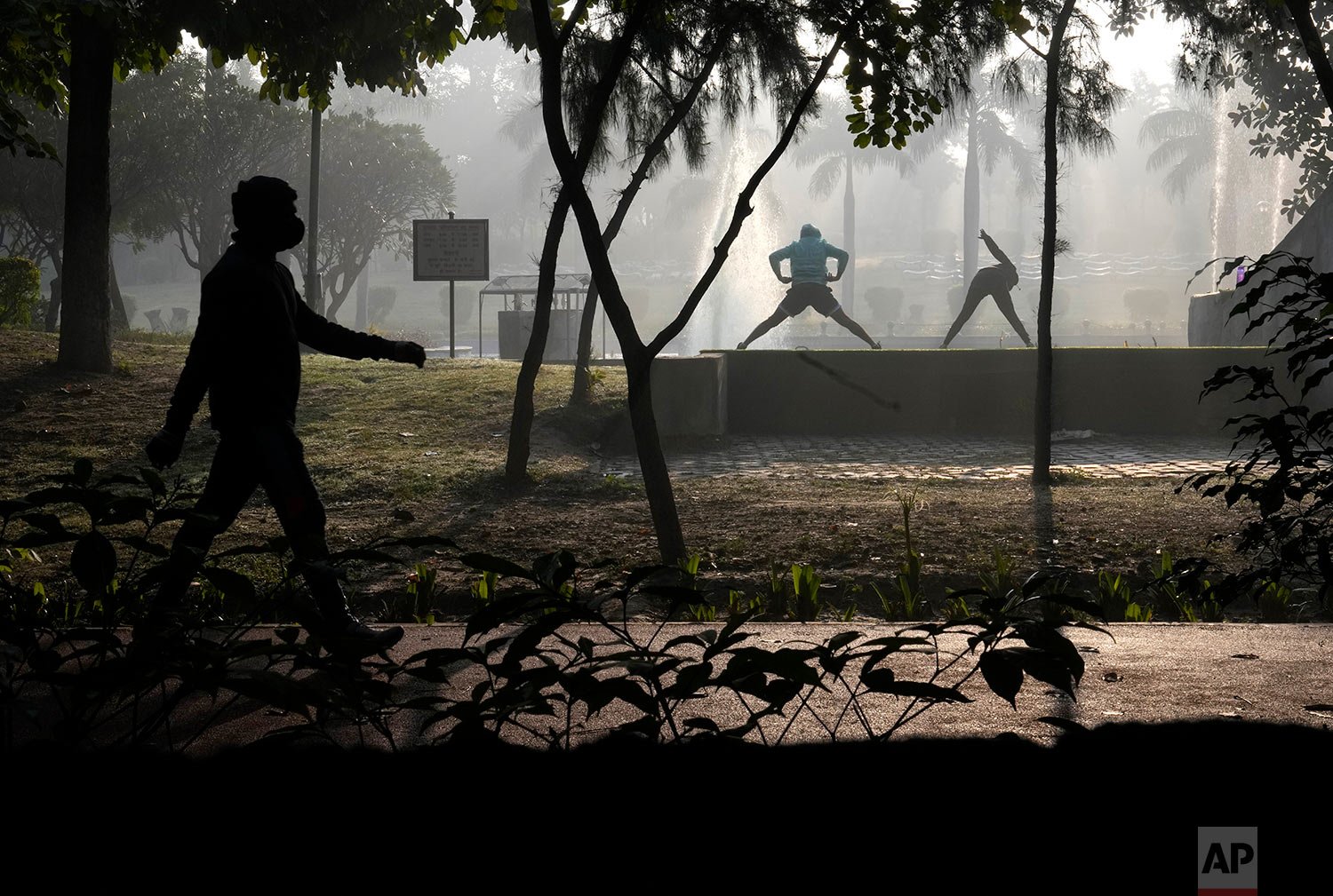  A man walks wearing a facemark as a precaution against the coronavirus as others exercise in a park, in New Delhi, India, Tuesday, Jan. 11, 2022. (AP Photo/Manish Swarup) 