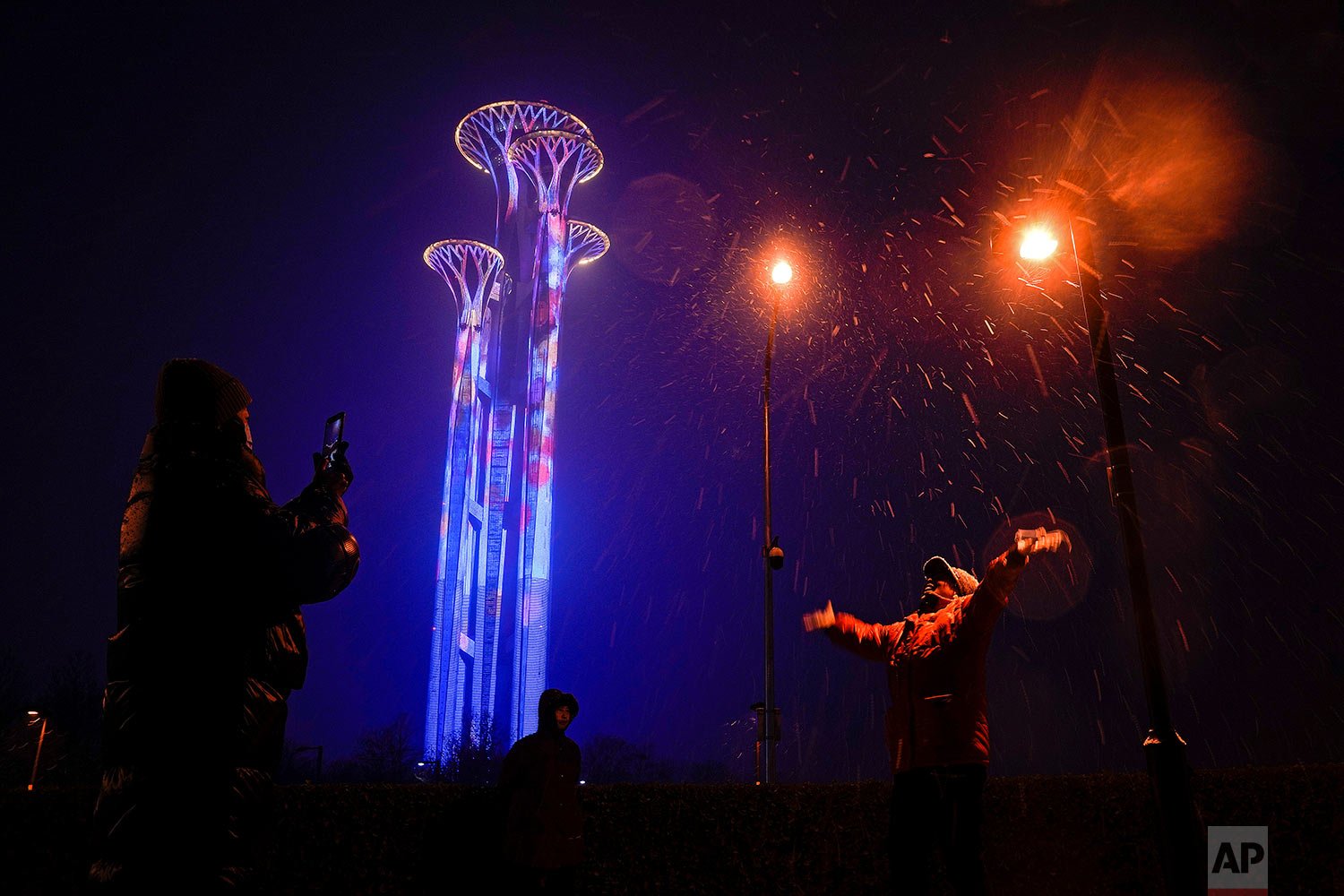  Residents film as snow falls near the illuminated Beijing Olympic Tower, at the 2022 Winter Olympics in Beijing, Sunday, Jan. 30, 2022. (AP Photo/Andy Wong) 