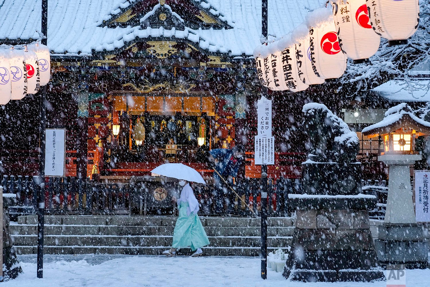  A shrine maiden walks past the main shrine while a worker clears the steps as the snow comes down Thursday, Jan. 6, 2022, in Tokyo. (AP Photo/Kiichiro Sato) 