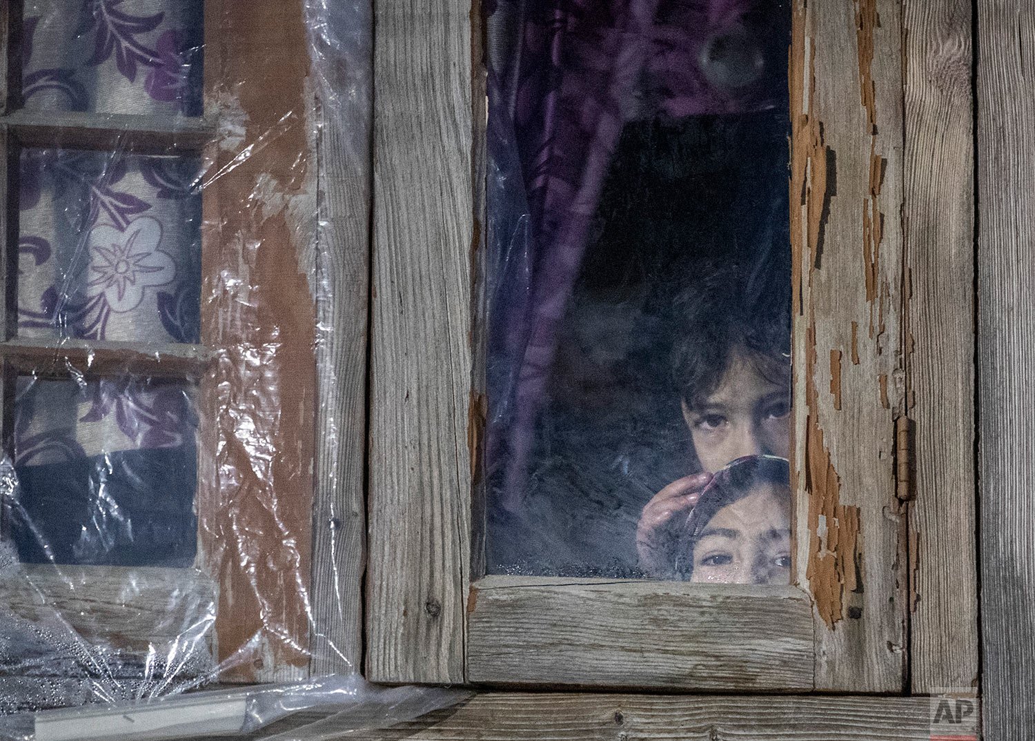  Kashmiri children look out from behind a closed window of their house during a counterinsurgency operation on the outskirts of Srinagar, Indian controlled Kashmir, Monday, Jan. 3, 2022.  (AP Photo/Mukhtar Khan) 