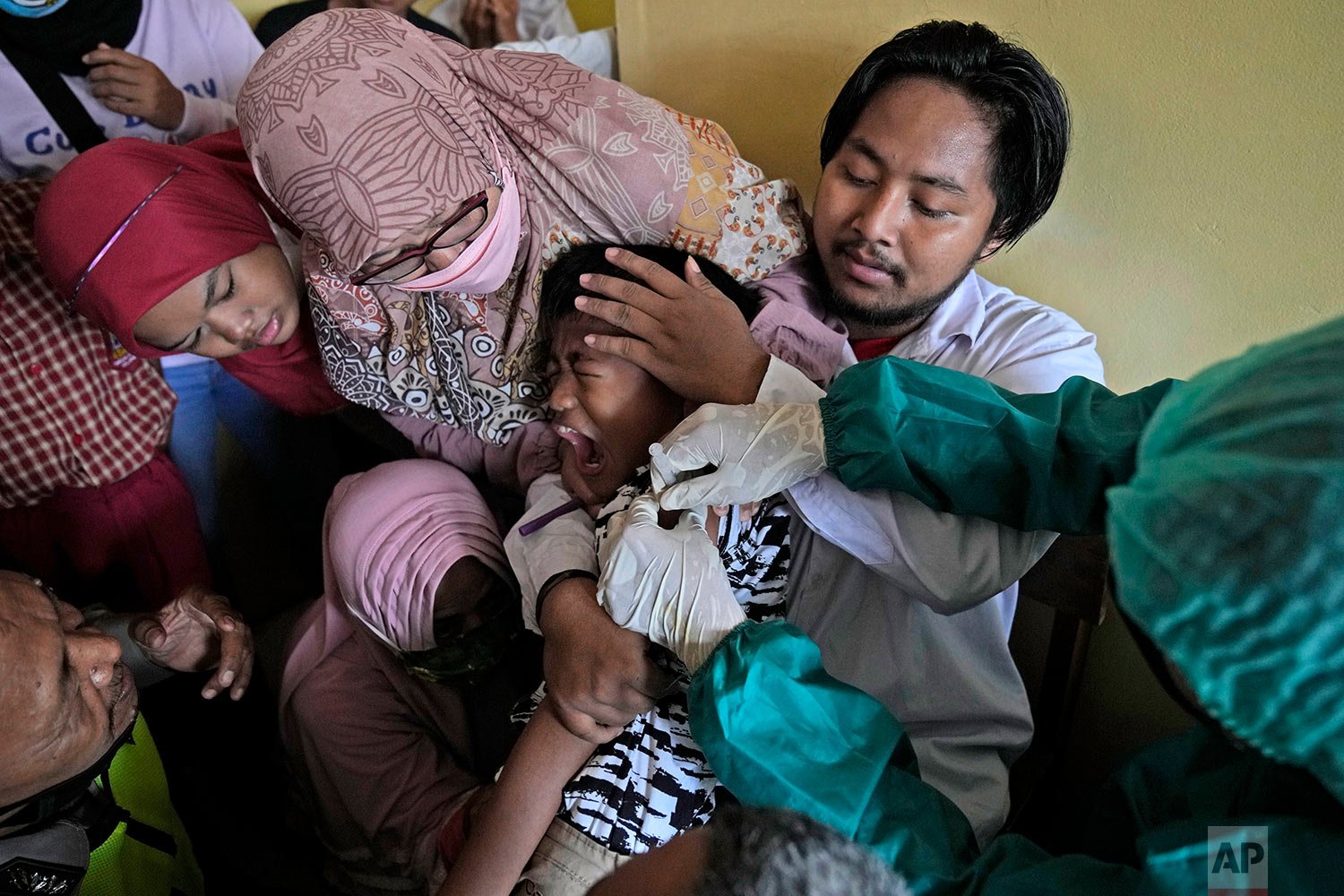  A parent, teachers and a police officer try to calm a student down as he receives a shot of the Sinovac COVID-19 vaccine during a vaccination campaign run by Indonesian National Police at a school for children with special needs in Depok on the outs