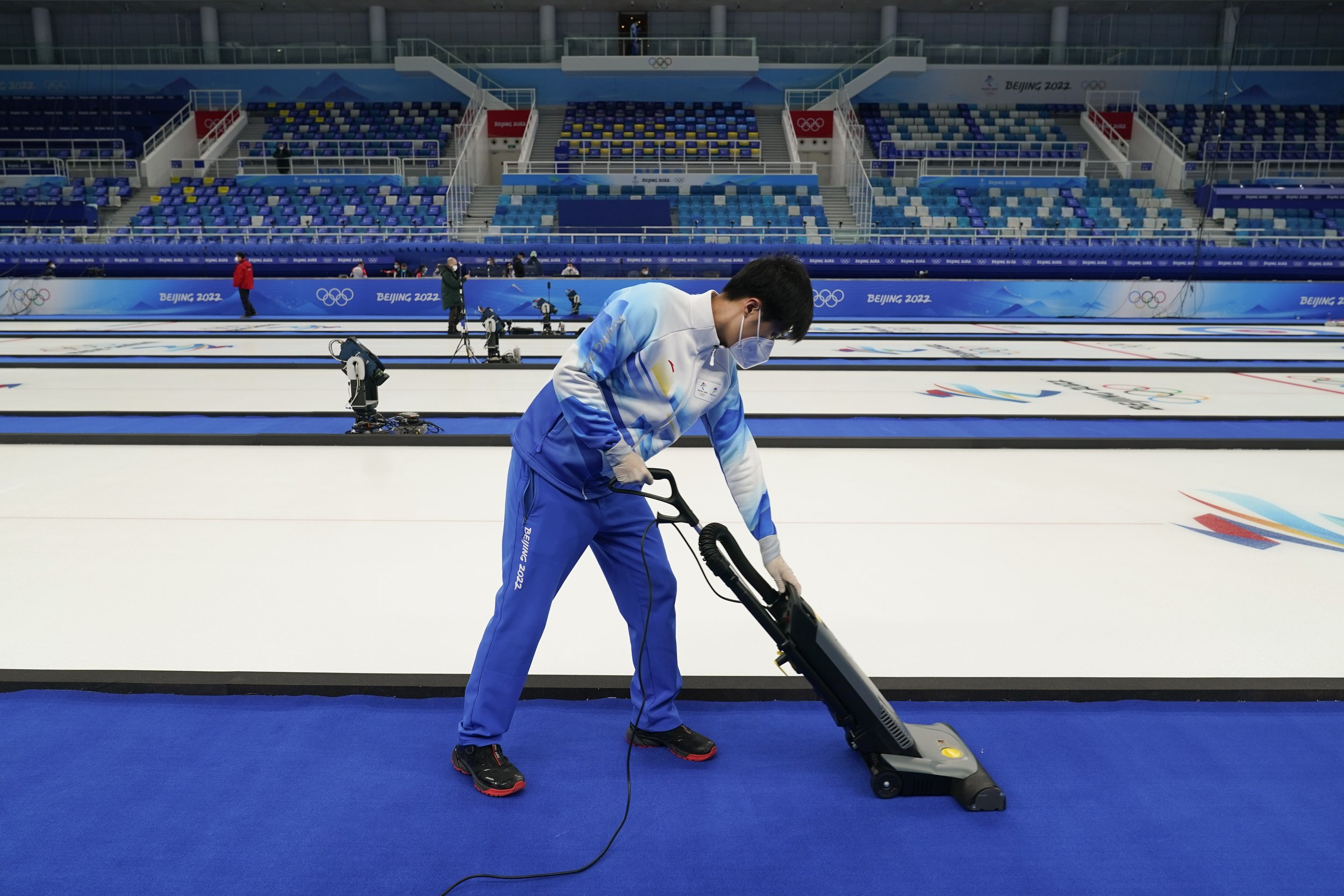  A volunteer vacuums the floor at the National Aquatics Center, a venue for curling events at the 2022 Winter Olympics, Saturday, Jan. 29, 2022, in Beijing. (AP Photo/Jae C. Hong) 