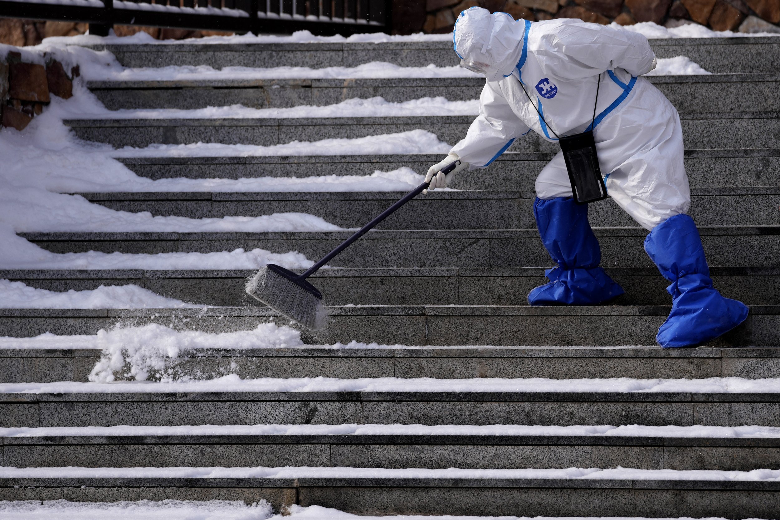  An Olympic worker in protective clothing clears snow from the steps at a hotel inside the Olympic bubble during the 2022 Winter Olympics, Saturday, Feb. 12, 2022, in Zhangjiakou, China. (AP Photo/Frank Augstein) 