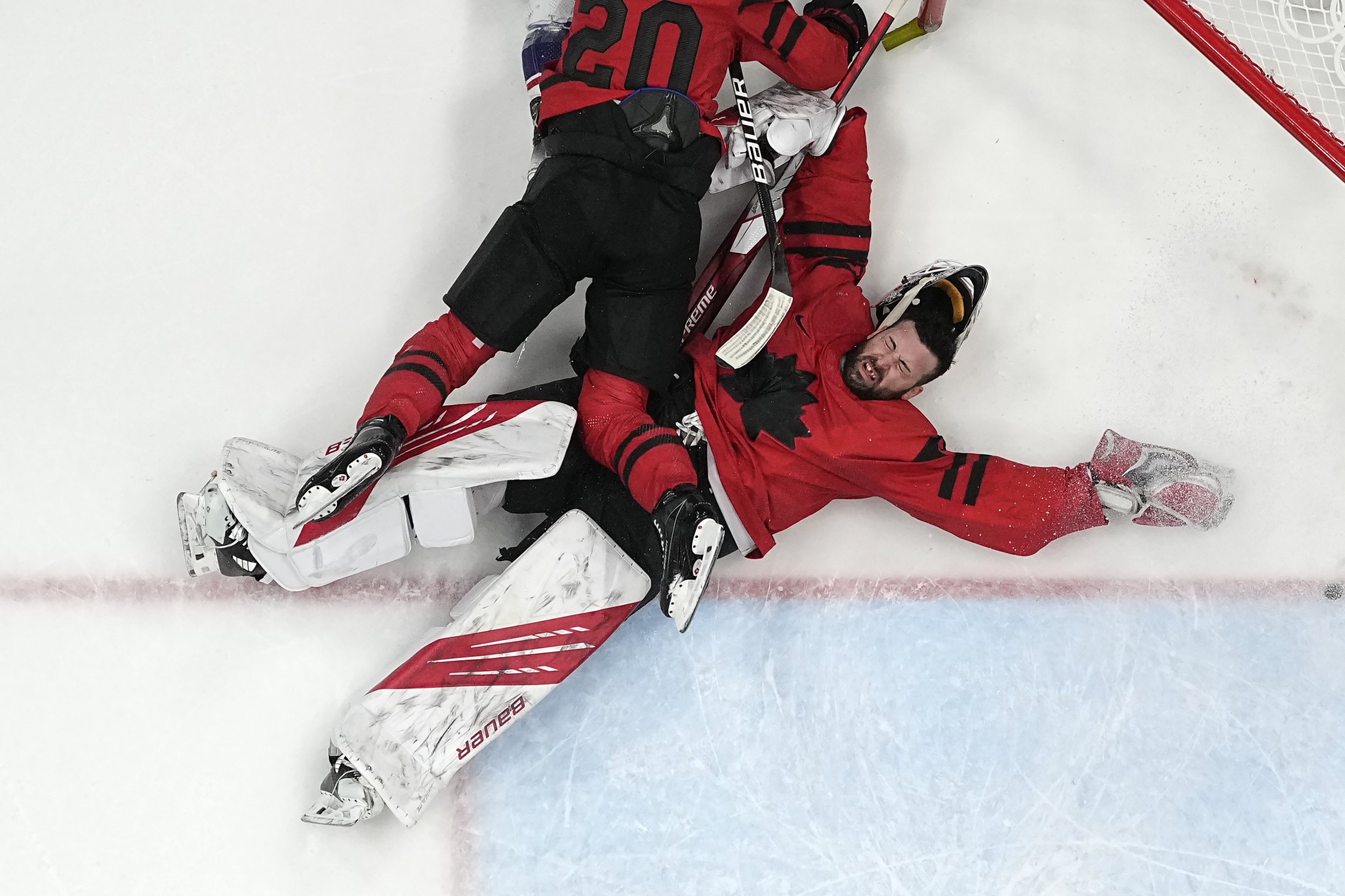  Canada goalkeeper Eddie Pasquale is knocked down by teammate Alex Grant (20) during a preliminary round men's hockey game against the United States at the 2022 Winter Olympics, Saturday, Feb. 12, 2022, in Beijing. (AP Photo/Matt Slocum) 