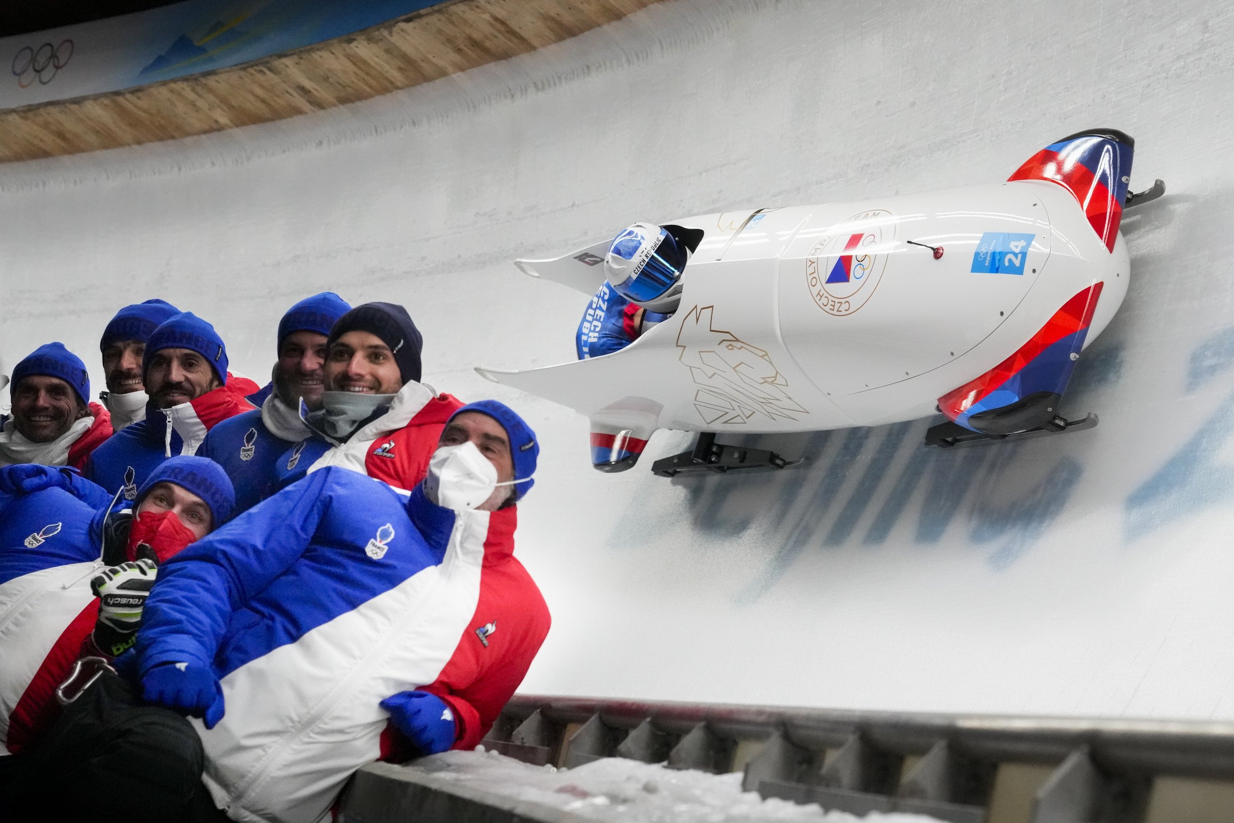  Members of the Czech Republic team pose for a photo as teammates Dominik Dvorak and Jakub Nosek slide past during the 2-man heat 1 at the 2022 Winter Olympics, Monday, Feb. 14, 2022, in the Yanqing district of Beijing. (AP Photo/Dmitri Lovetsky) 