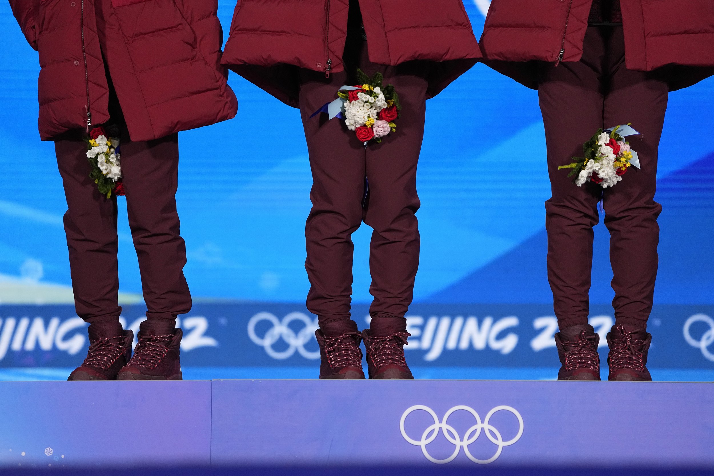  Canadian athletes hold their bouquets between their legs to wear their face masks during the medal ceremony for the men's 5000-meters relay short track speedskating at the 2022 Winter Olympics, Thursday, Feb. 17, 2022, in Beijing. (AP Photo/Jae C. H