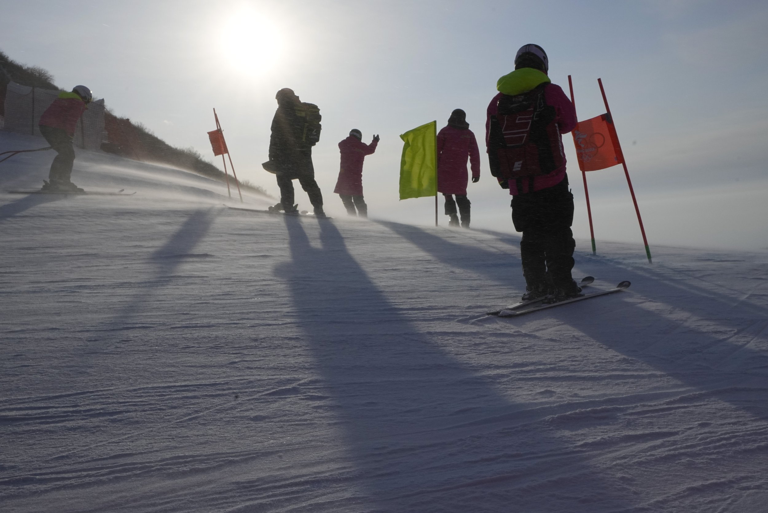  Officials stand on the course as a gust of wind blows powder across the slopes of the course for the women's combined downhill at the 2022 Winter Olympics, Thursday, Feb. 17, 2022, in the Yanqing district of Beijing. (AP Photo/Robert F. Bukaty) 