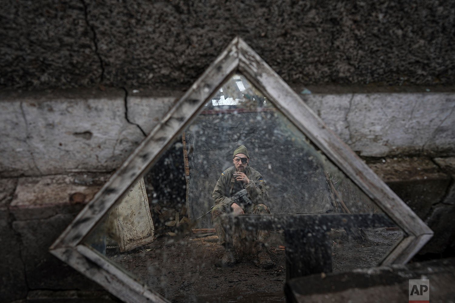  A Ukrainian serviceman is reflected in a mirror as he smokes a cigarette on a position at the line of separation between Ukraine-held territory and rebel-held territory near Zolote, Ukraine, Saturday, Feb. 19, 2022.  (AP Photo/Evgeniy Maloletka) 