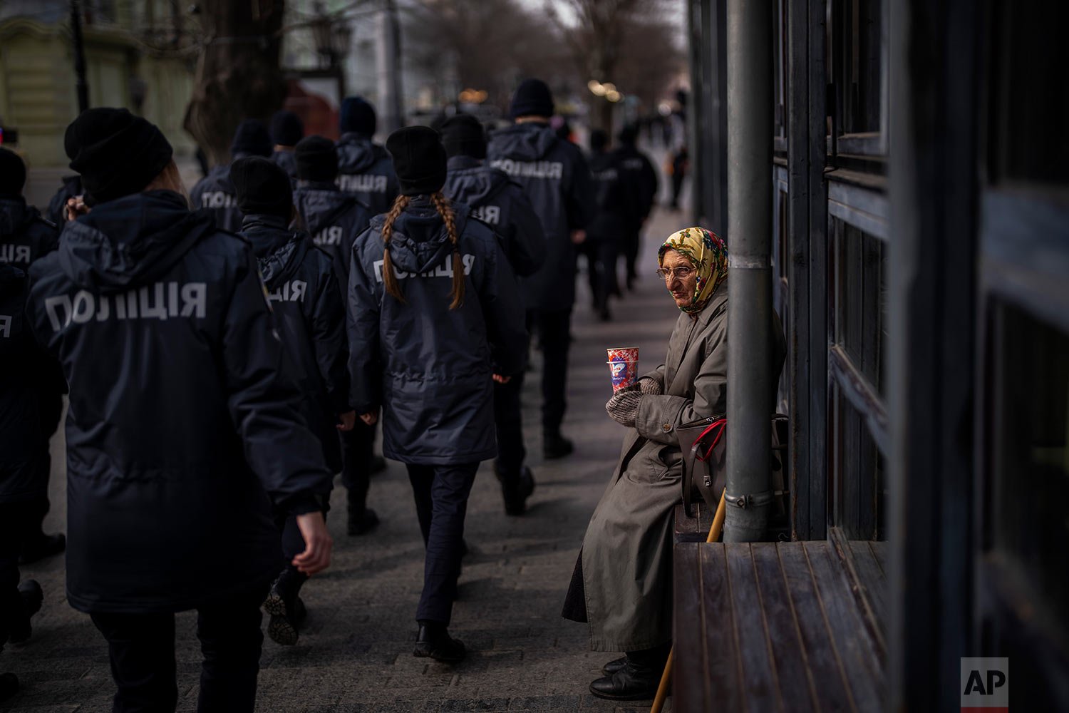  Ukrainian police officers march past a woman begging for alms during a demonstration in Odessa, Ukraine, Sunday, Feb. 20, 2022.  (AP Photo/Emilio Morenatti) 