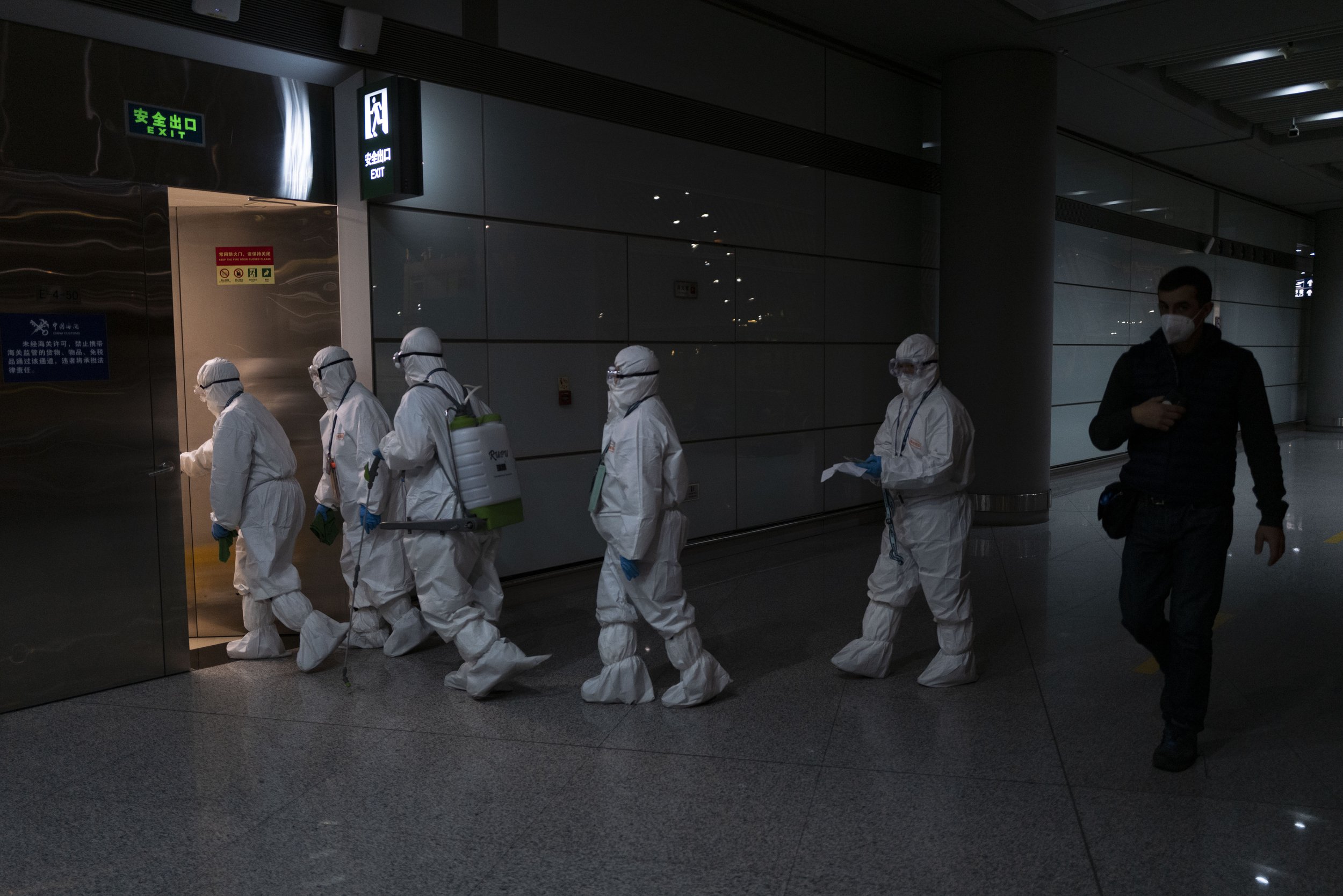  A passenger walks past airport employees in protective gear at the Beijing Capital International Airport at the 2022 Winter Olympics, Monday, Feb. 21, 2022, in Beijing. (AP Photo/Jae C. Hong) 