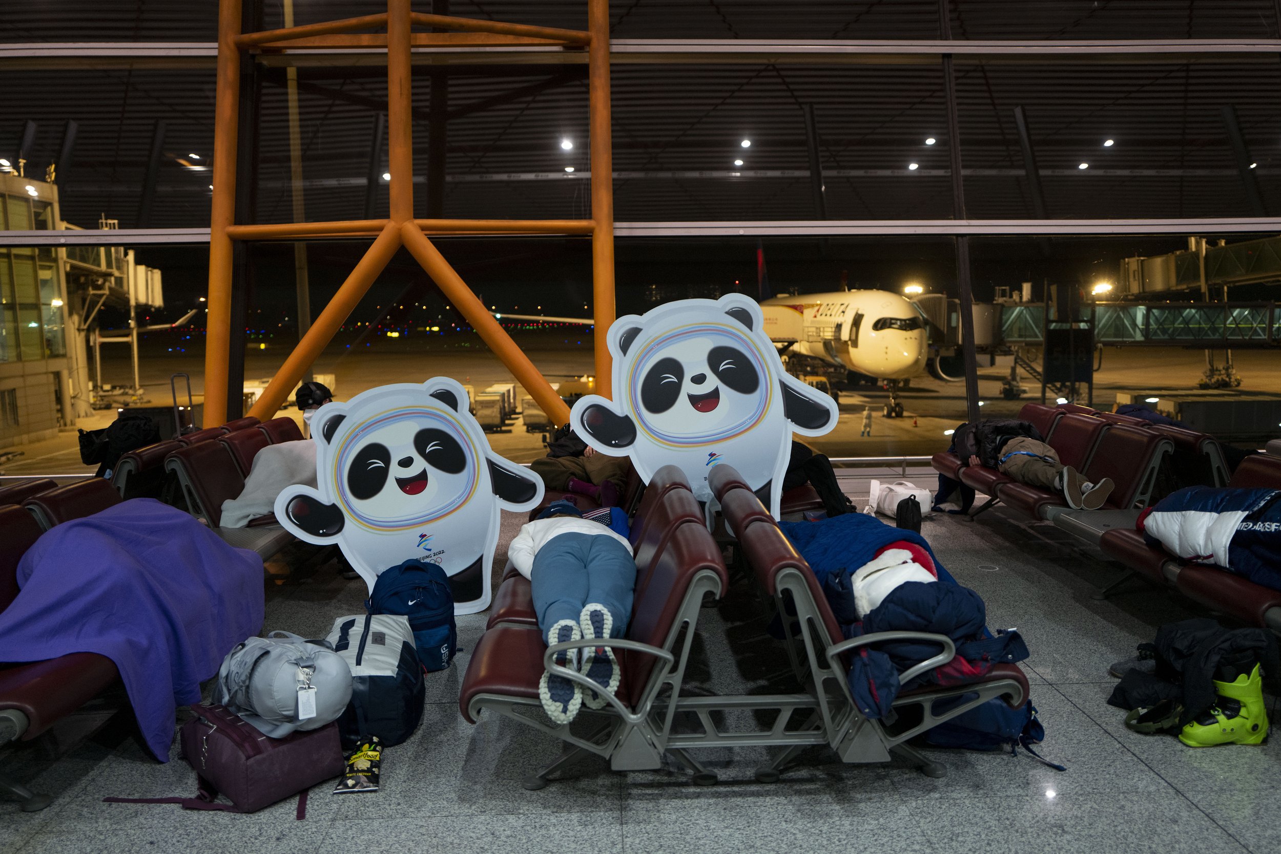  People sleep on benches next to cutouts of the Olympic mascot Bing Dwen Dwen at the Beijing Capital International Airport after the 2022 Winter Olympics, Monday, Feb. 21, 2022, in Beijing. (AP Photo/Jae C. Hong) 