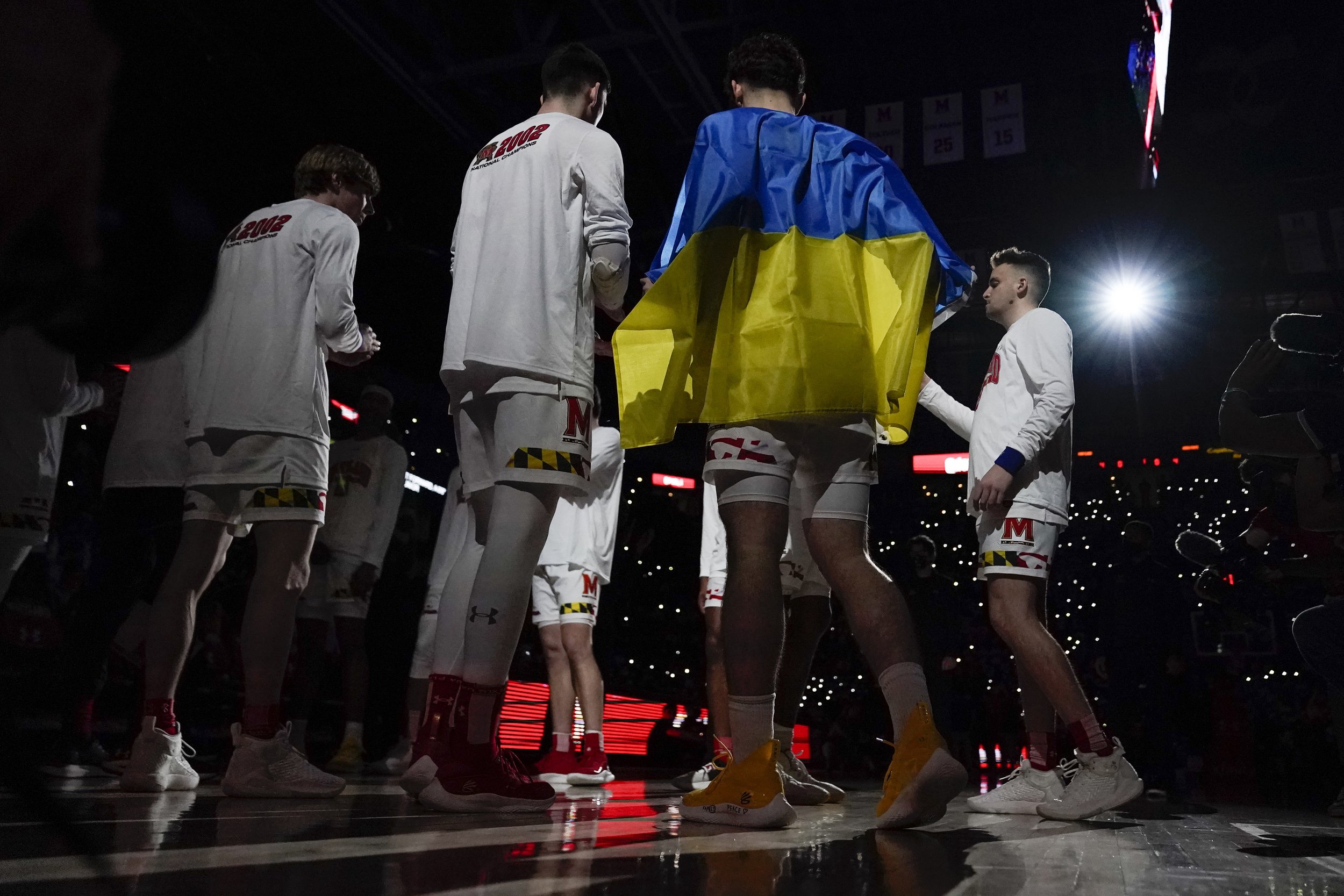 Maryland forward Pavlo Dziuba, front right, who was born in Kyiv, Ukraine, is draped in a flag of Ukraine prior to an NCAA college basketball game against Ohio State, Sunday, Feb. 27, 2022, in College Park, Md. (AP Photo/Julio Cortez) 