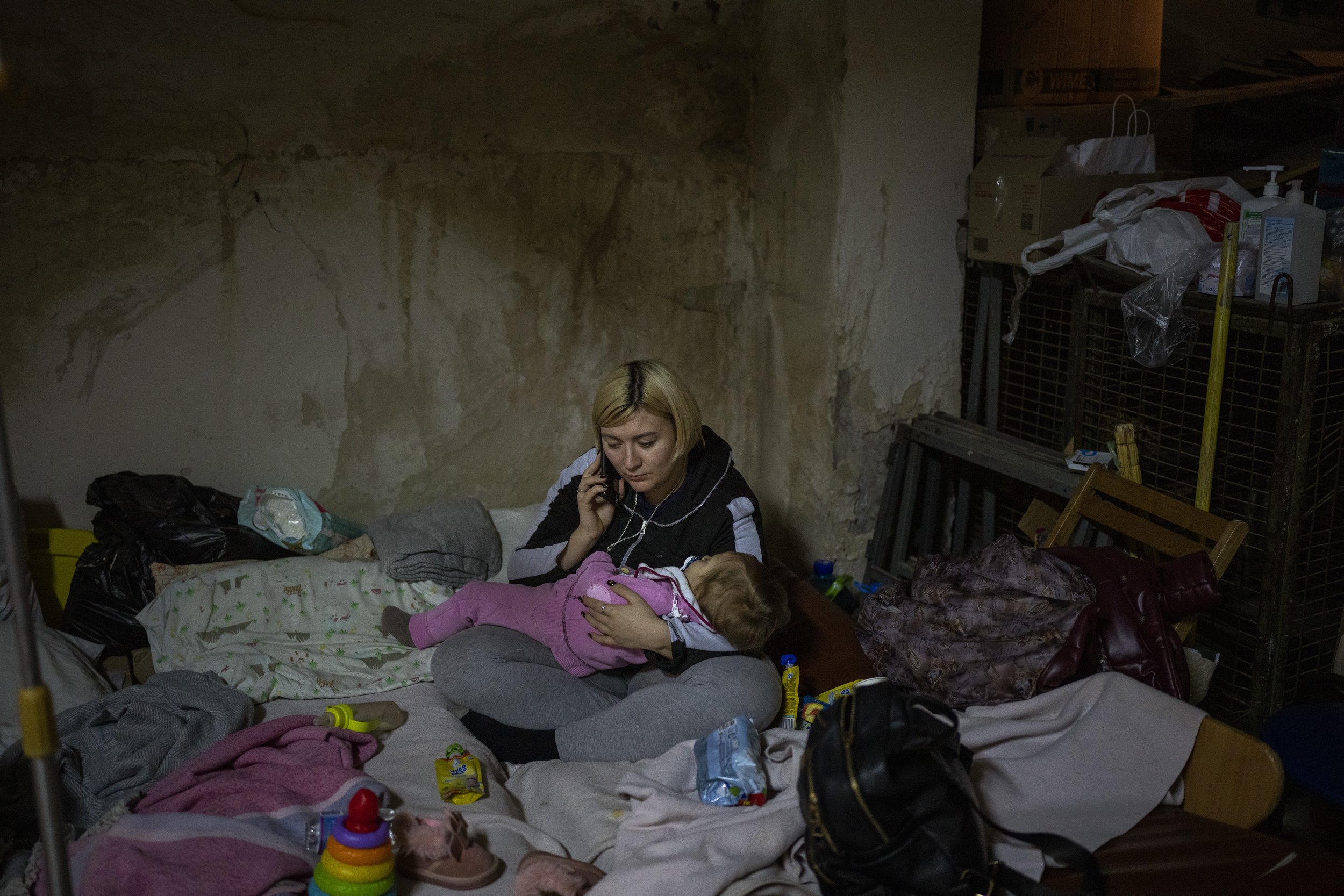  A woman speaks by phone holding her sick baby in a basement used as a bomb shelter at the Okhmadet children's hospital in central Kyiv, Ukraine, Tuesday, March 1. 2022. (AP Photo/Emilio Morenatti) 