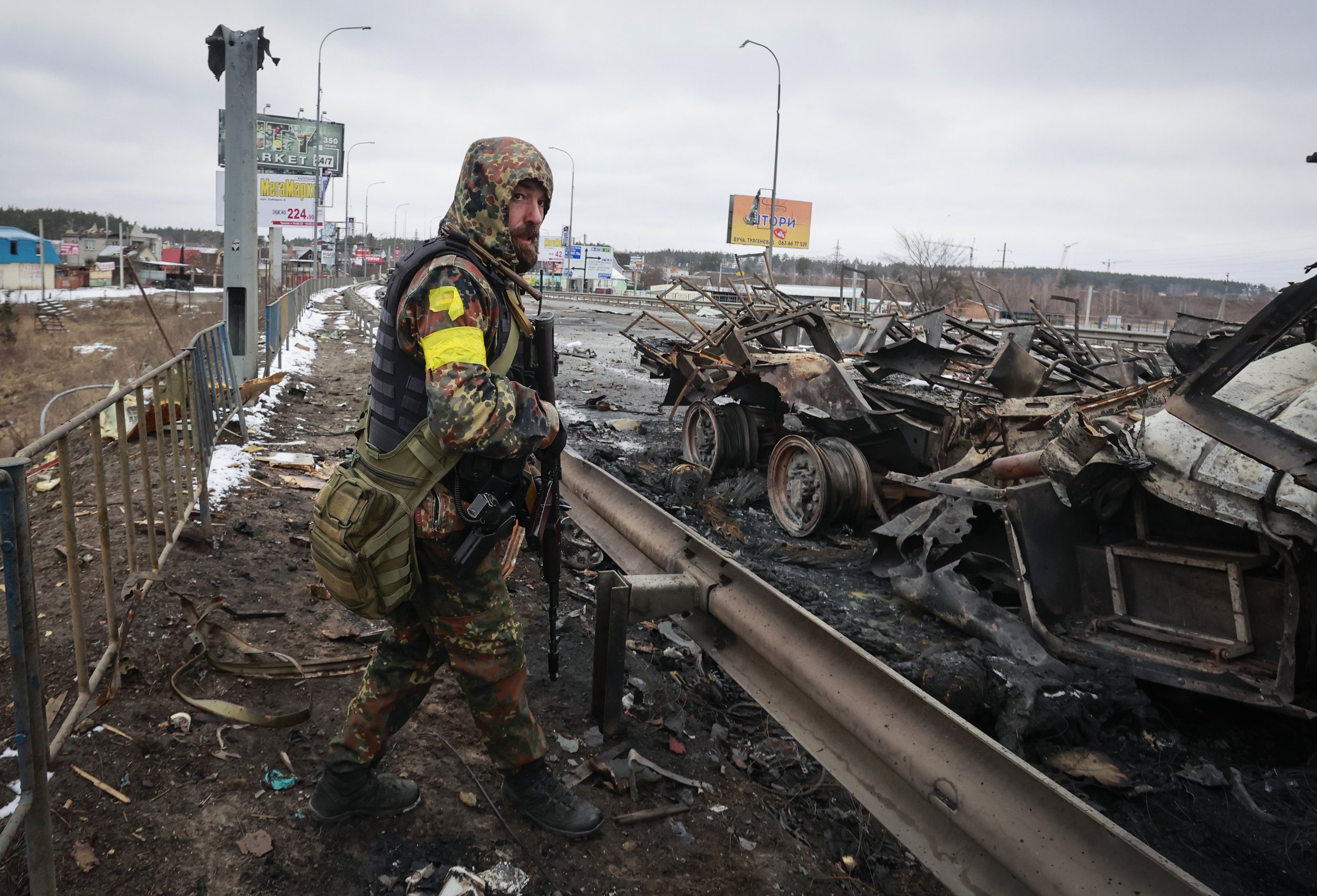  An armed man stands by the remains of a Russian military vehicle in Bucha, close to the capital Kyiv, Ukraine, Tuesday, March 1, 2022. (AP Photo/Serhii Nuzhnenko) 