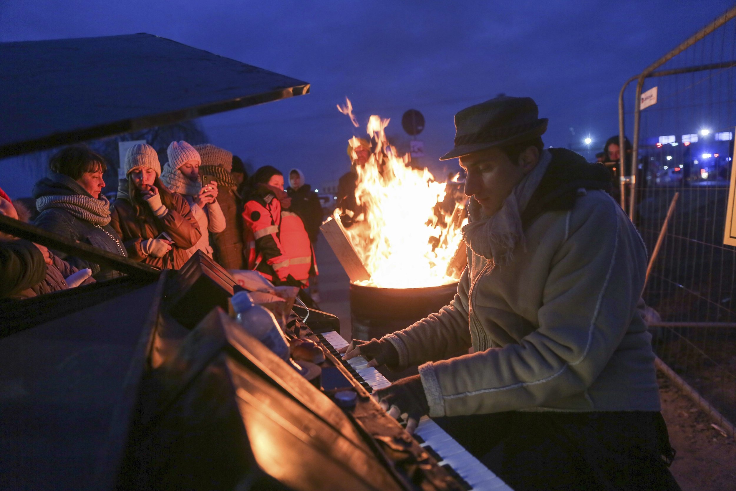 People gather around Italian pianist Davide Mortarelli who is performing for the refugees fleeing war in Ukraine at the border crossing Medyka, Poland, Friday, March 4, 2022. (AP Photo/Visar Kryeziu)