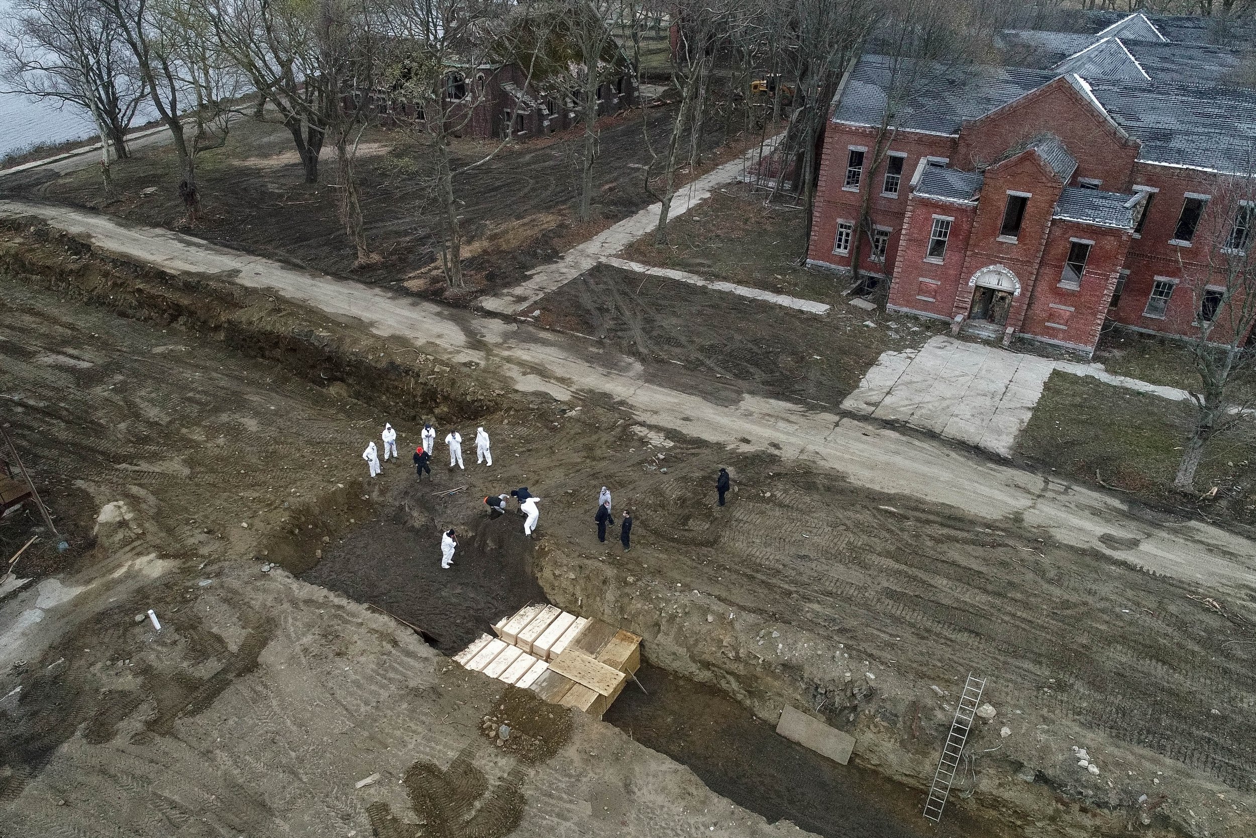  Workers wearing personal protective equipment bury bodies in a trench on Hart Island, Thursday, April 9, 2020, in the Bronx borough of New York. (AP Photo/John Minchillo) 