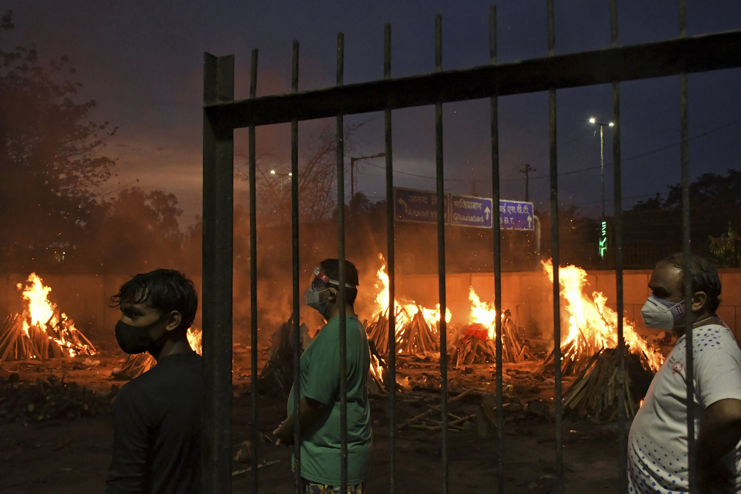  People watch burning funeral pyres of their relatives who died of COVID-19 in a ground that has been converted into a crematorium in New Delhi, India, Thursday, May 6, 2021. Infections in India hit another grim daily record on Thursday as demand for