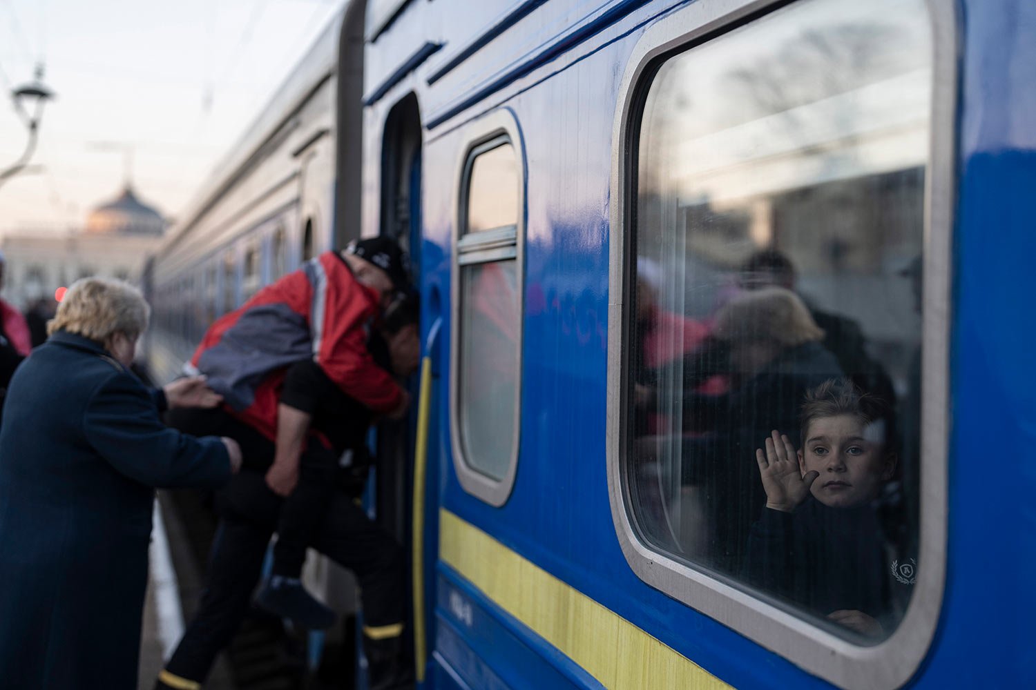  A child waves through the window of a train as people step on at the train station in Odesa, southern Ukraine, on Wednesday, March 23, 2022. (AP Photo/Petros Giannakouris) 