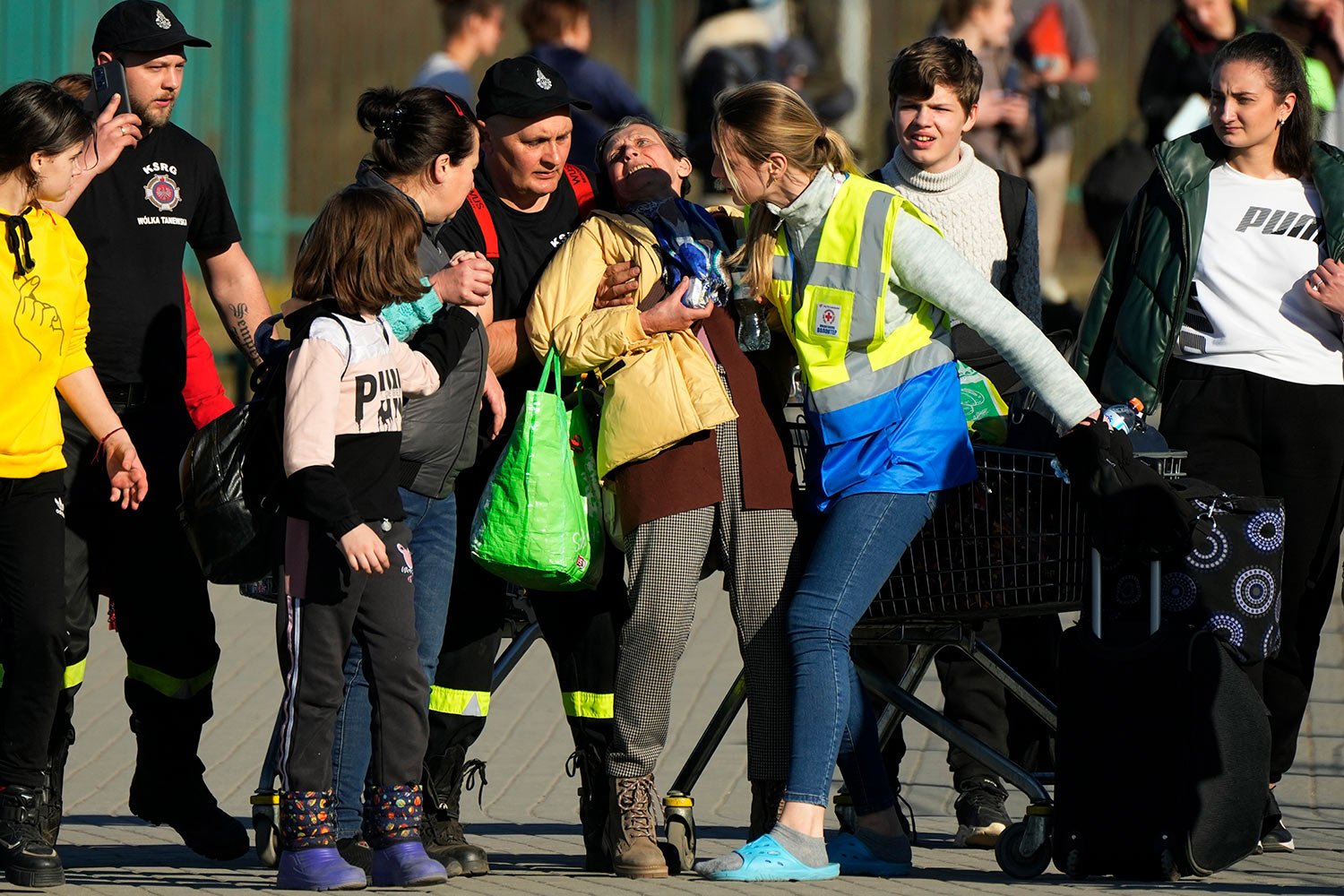  A woman losing her consciousness, receives help from Polish paramedics as other Ukrainian refugees pass the border crossing in Medyka, southeastern Poland, on Wednesday, March 23, 2022. (AP Photo/Sergei Grits) 