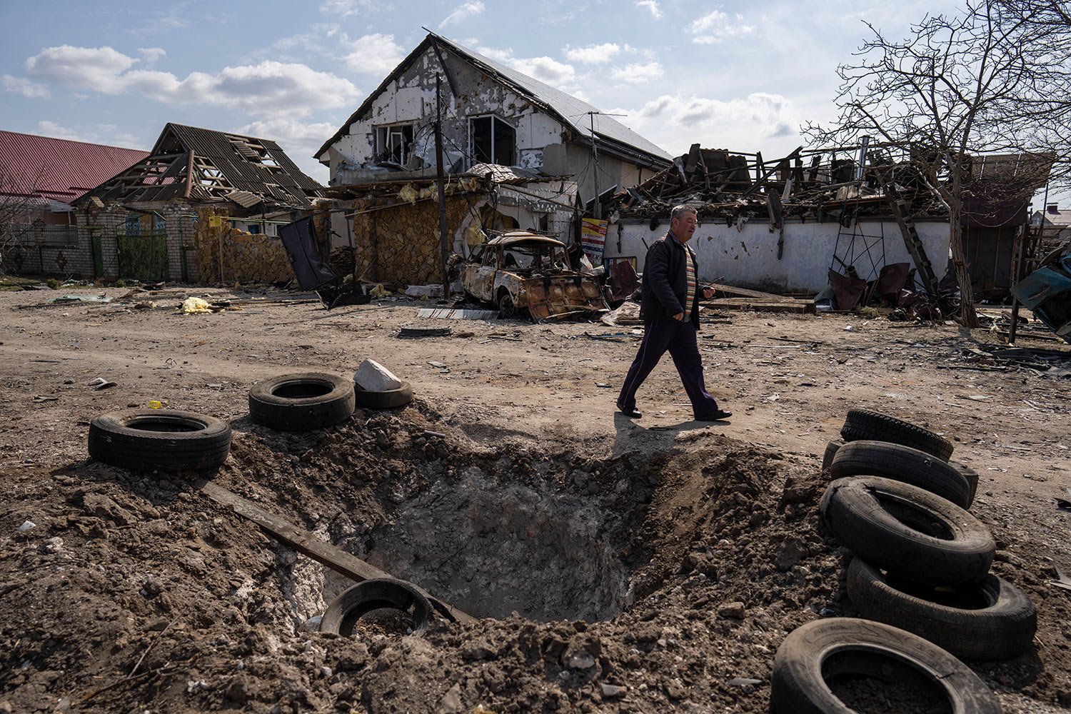  A man walks behind a crater created by a bomb and in front of damaged houses following a Russian bombing earlier this week, outskirts Mykolaiv, Ukraine, Friday, 25, 2022.(AP Photo/Petros Giannakouris) 