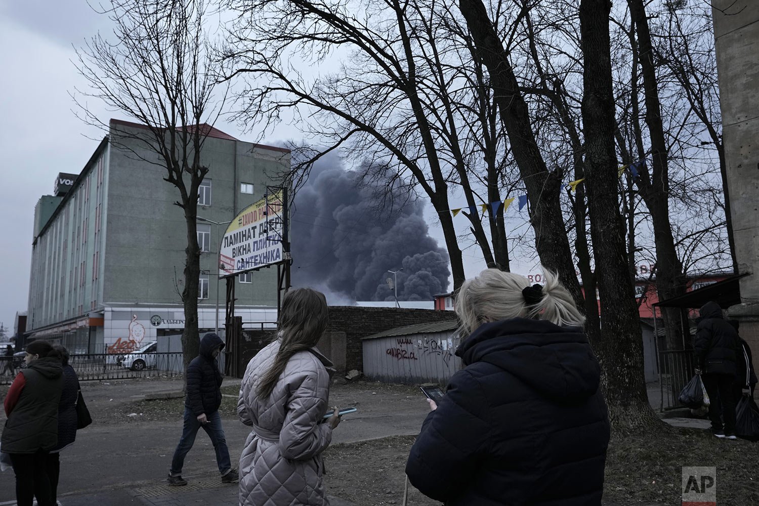  People watch smoke rising behind buildings following explosions in Lviv, western Ukraine, Saturday, March 26, 2022. (AP Photo/Nariman El-Mofty) 