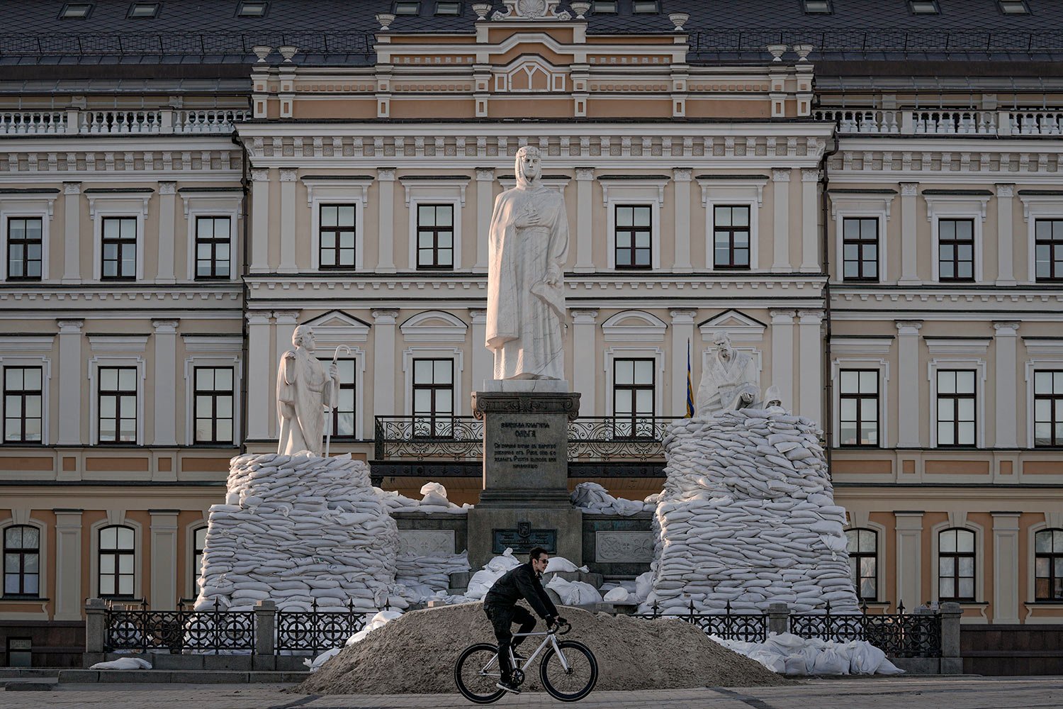  A man rides a bicycle backdropped by a statue of Grand Princess Olga of Kyiv, in the process of being covered in sandbags to avoid damage from potential shelling, in Kyiv, Ukraine, Monday, March 28, 2022. (AP Photo/Vadim Ghirda) 
