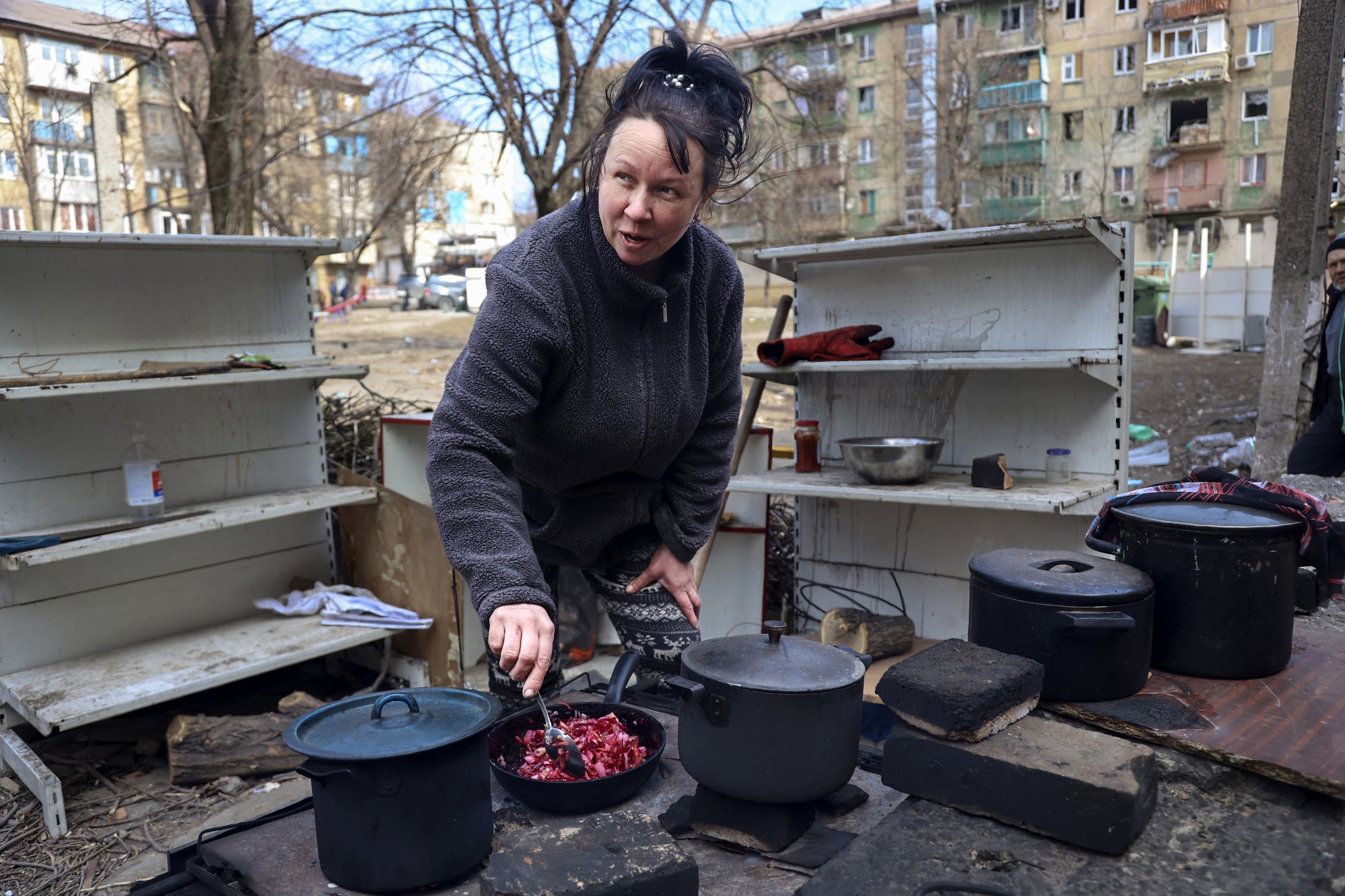  A woman cooks in a yard of apartment buildings damaged by shelling from fighting on the outskirts of Mariupol, Ukraine, in territory under control of the separatist government of the Donetsk People's Republic, on Tuesday, March 29, 2022. (AP Photo/A