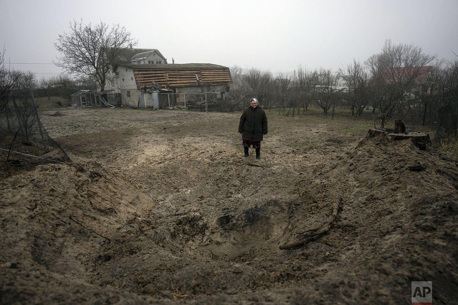  Zina, 65, stands next to a crater created after a bomb hit the ground behind her house on the outskirts of Kyiv, Ukraine, Friday, April 1, 2022. (AP Photo/Rodrigo Abd) 