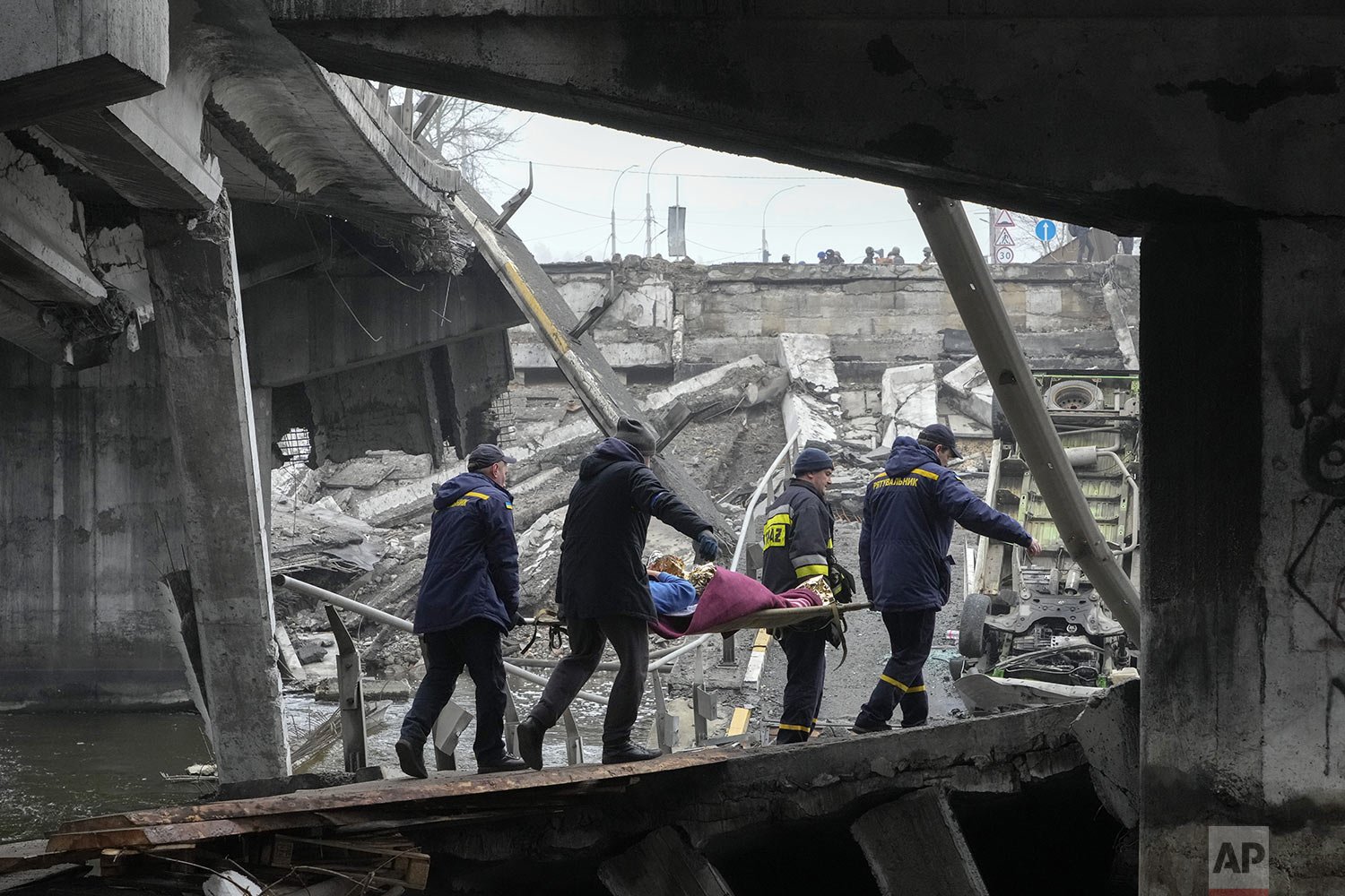  Ukrainian rescue workers carry an elderly woman under a destroyed bridge in Irpin, close to Kyiv, Ukraine, Friday, April 1, 2022. (AP Photo/Efrem Lukatsky) 