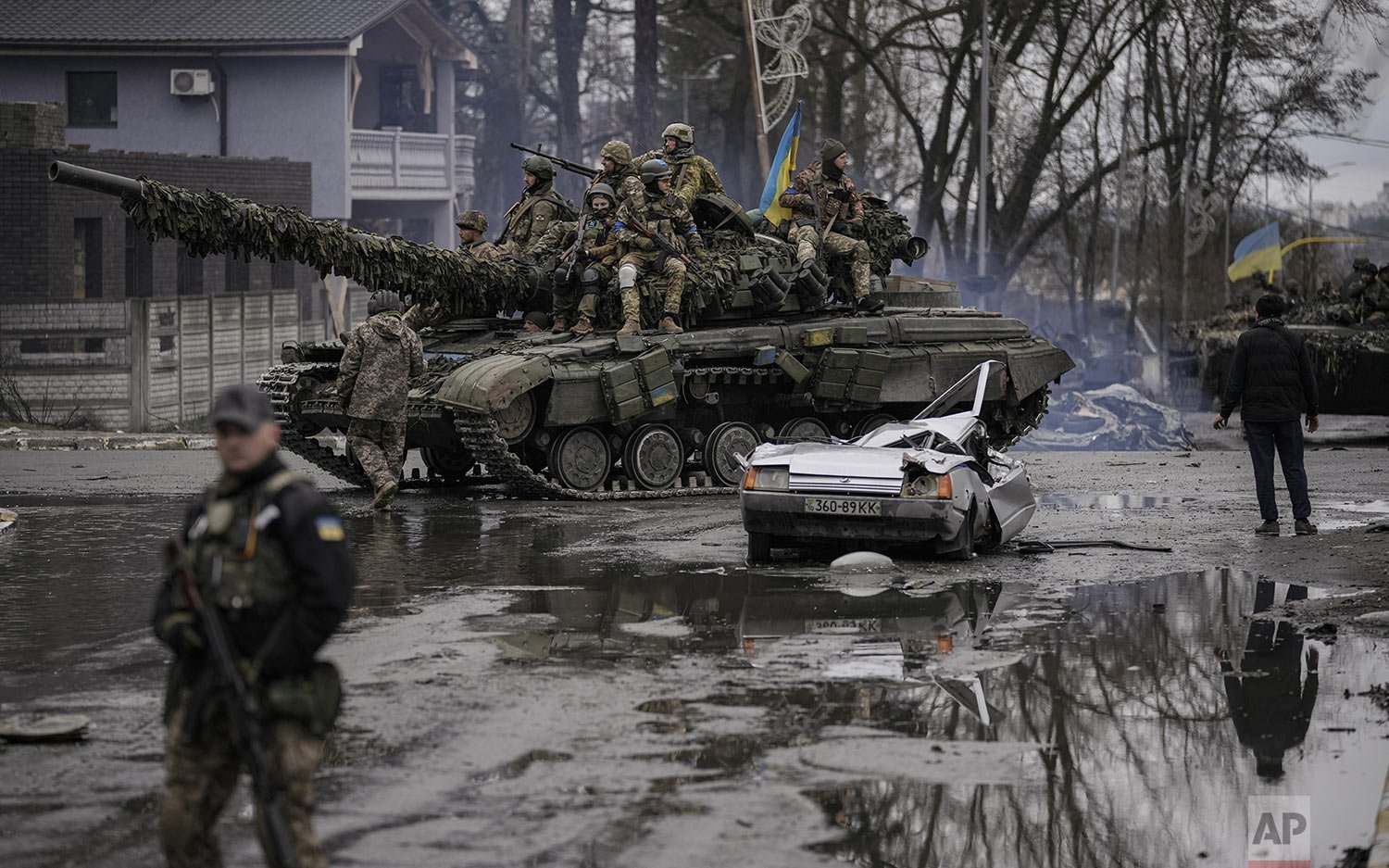  A man stands next to a civilian vehicle that was destroyed during fighting between Ukrainian and Russian forces that still contains the body of the driver as Ukrainian servicemen ride on a tank vehicle outside Kyiv, Ukraine, Saturday, April 2, 2022.