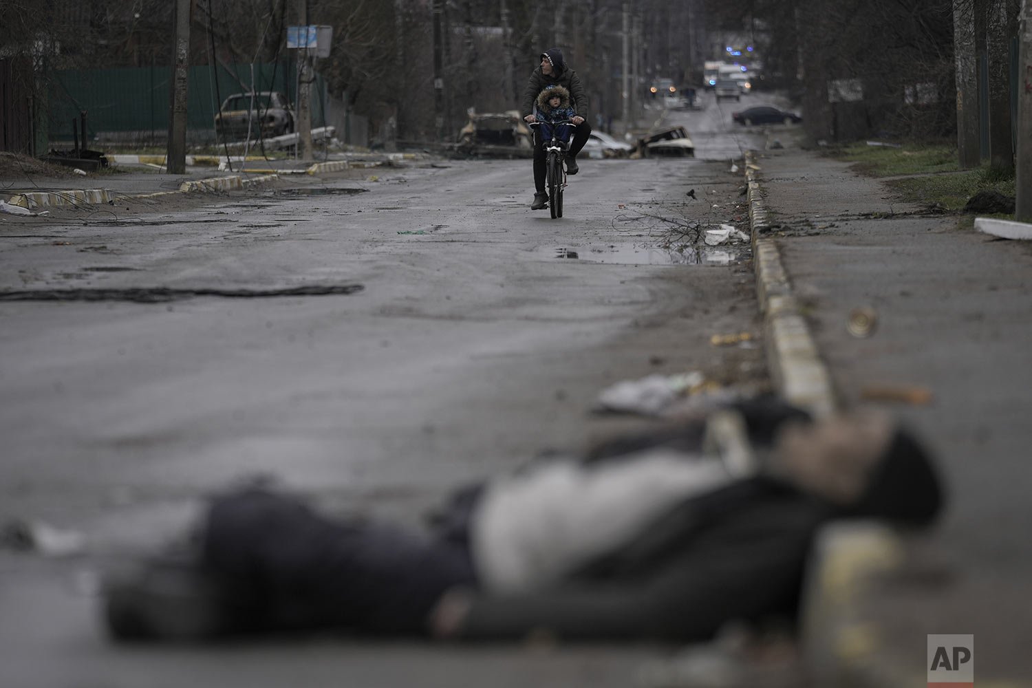  A man and child on a bicycle come across the body of a civilian lying on a street in the formerly Russian-occupied Kyiv suburb of Bucha, Ukraine, Saturday, April 2, 2022. (AP Photo/Vadim Ghirda) 