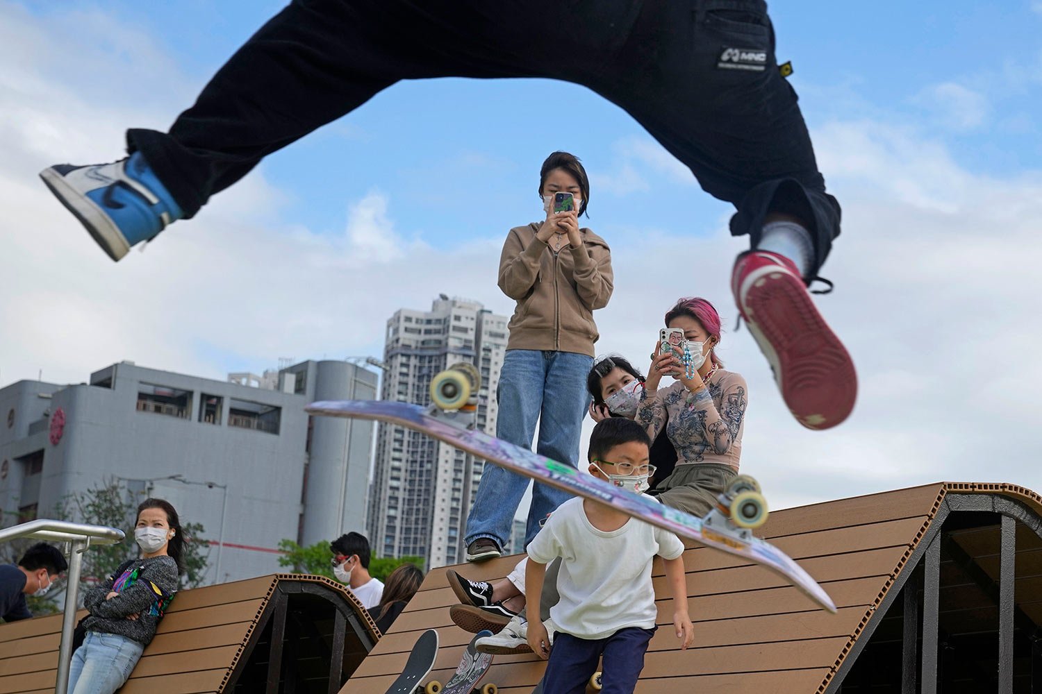  Kids wearing face masks to help protect from the coronavirus watch a teenager flipping his skateboard in an "ollie" at a park in Hong Kong, Wednesday, March 30, 2022. (AP Photo/Kin Cheung) 