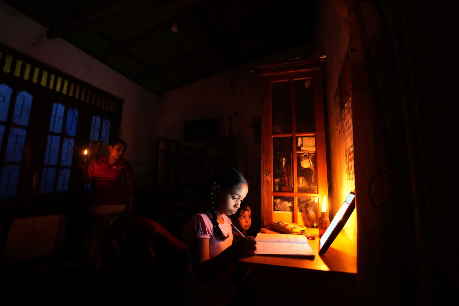  A girl uses a kerosine oil lamp to attend online lessons during a power cut in Colombo, Sri Lanka, Friday, March 4, 2022.  (AP Photo/Eranga Jayawardena, File) 
