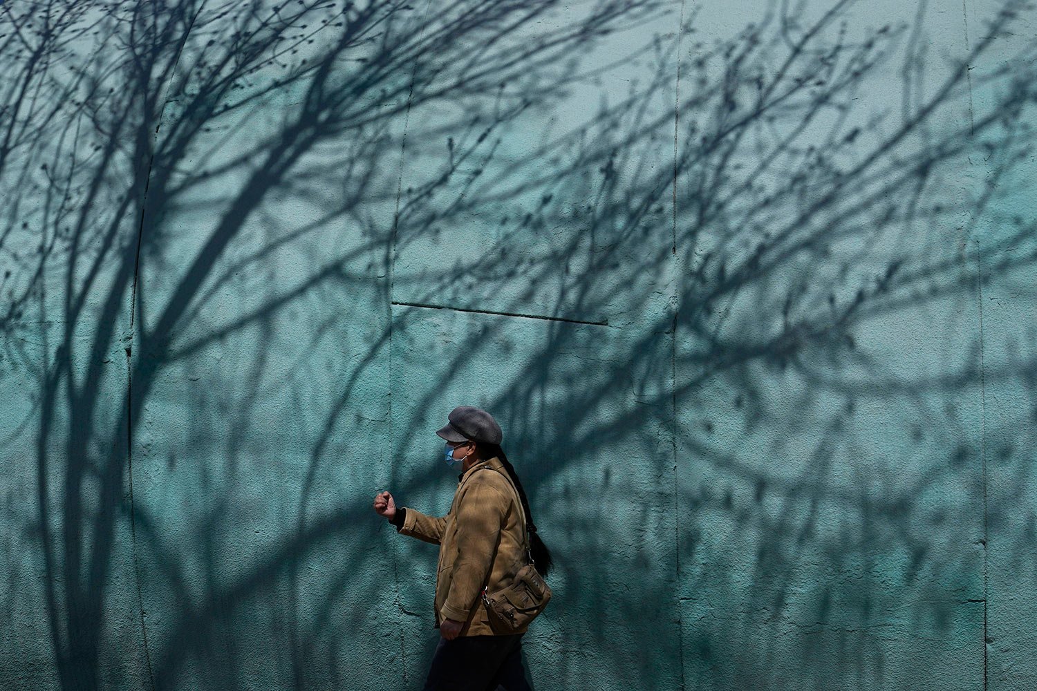  A resident wearing a mask walks past shadows of a tree in a park on Thursday, March 31, 2022, in Beijing.  (AP Photo/Ng Han Guan) 