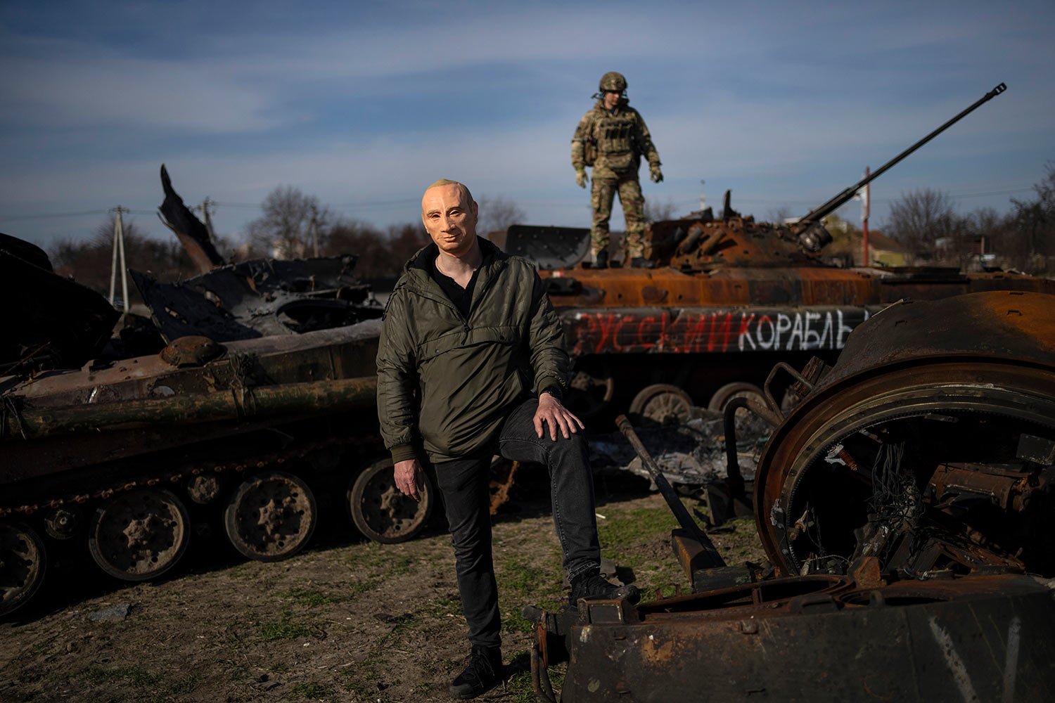  A man poses for the picture wearing a mask of Russian President Vladimir Putin, while a Ukrainian soldier stands on top of a destroyed Russian tank in Bucha, on the outskirts of Kyiv, Ukraine, Thursday, April 7, 2022. (AP Photo/Rodrigo Abd) 