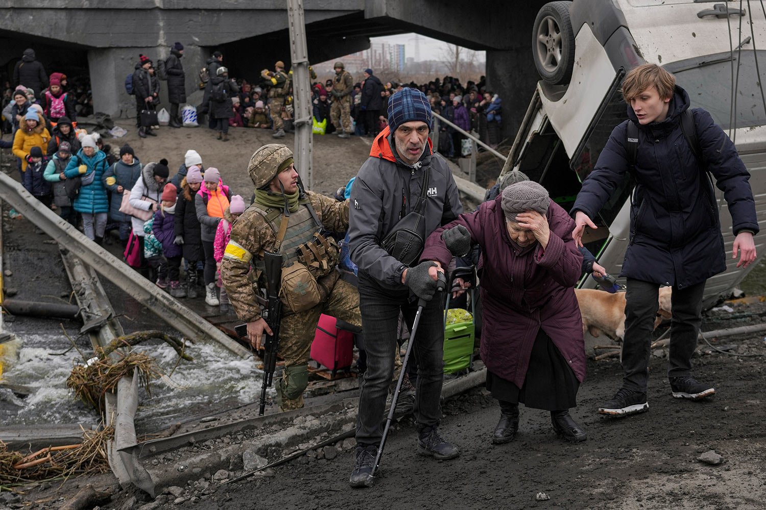  An elderly lady gets assisted while crossing the Irpin river, under a bridge that was destroyed, as civilians flee the town of Irpin, Ukraine, Saturday, March 5, 2022. (AP Photo/Vadim Ghirda) 
