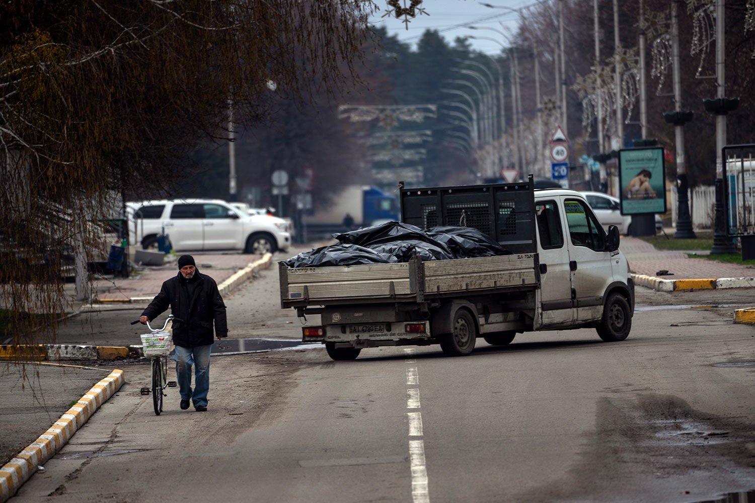  A man walks with a bicycle next to a truck that carries black bags with corpses of people killed during the war with Russia and exhumed from a mass grave for investigations in Bucha, on the outskirts of Kyiv, Ukraine, Monday, April 11, 2022. (AP Pho