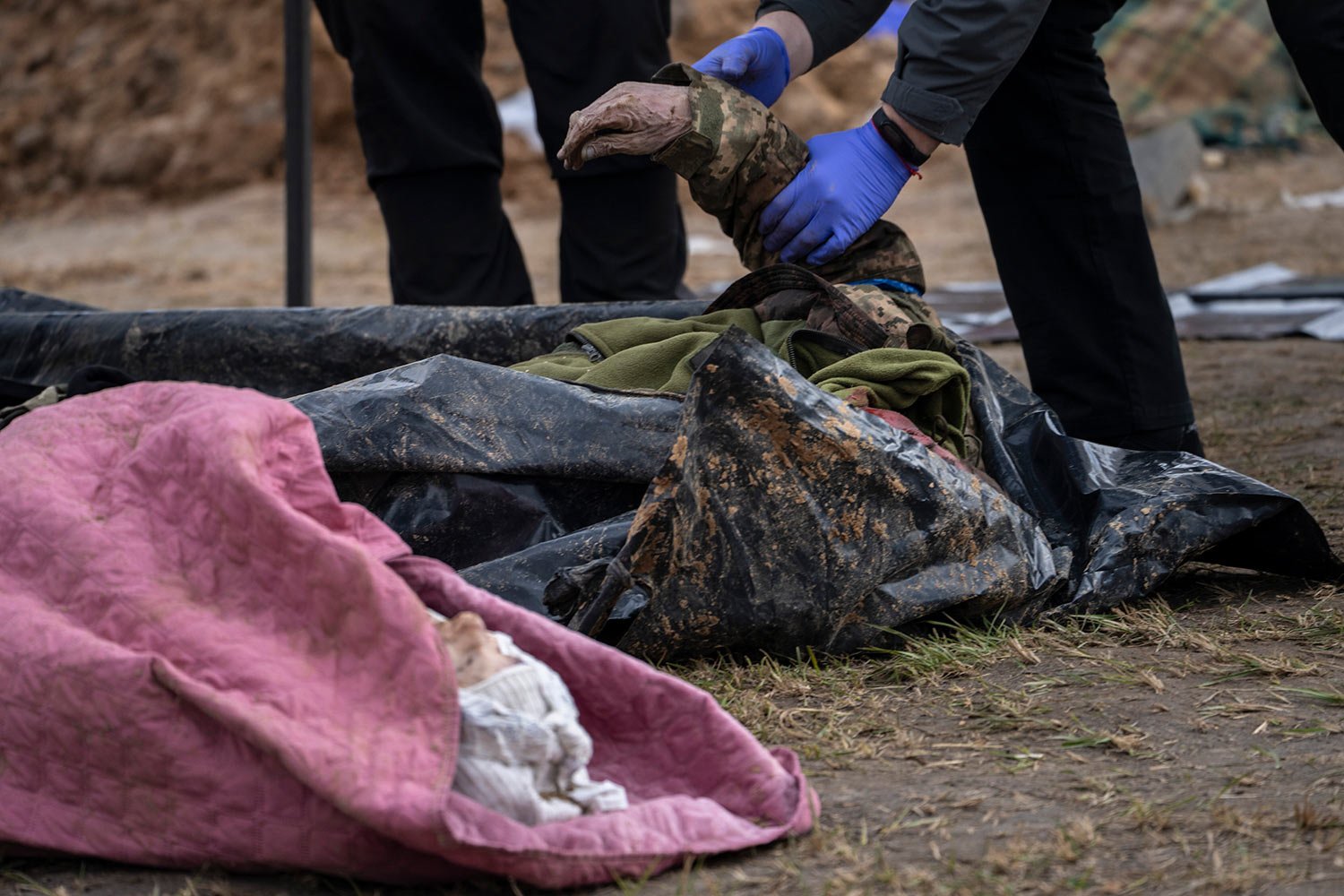  A policeman examines the corpse of a Ukrainian soldier removed from a mass grave in Bucha, on the outskirts of Kyiv, Ukraine, Monday, April 11, 2022. (AP Photo/Rodrigo Abd) 