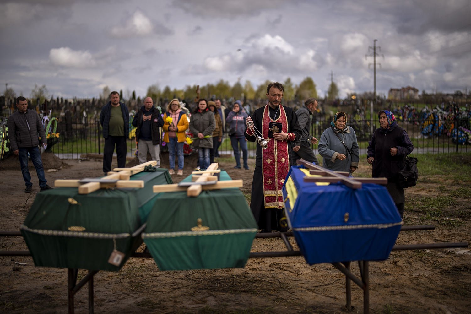  A priest blesses the remains of three people who died during the Russian invasion and were disinterred from temporary burial sites in Bucha, on the outskirts of Kyiv, Ukraine, Wednesday, April 27, 2022. (AP Photo/Emilio Morenatti) 