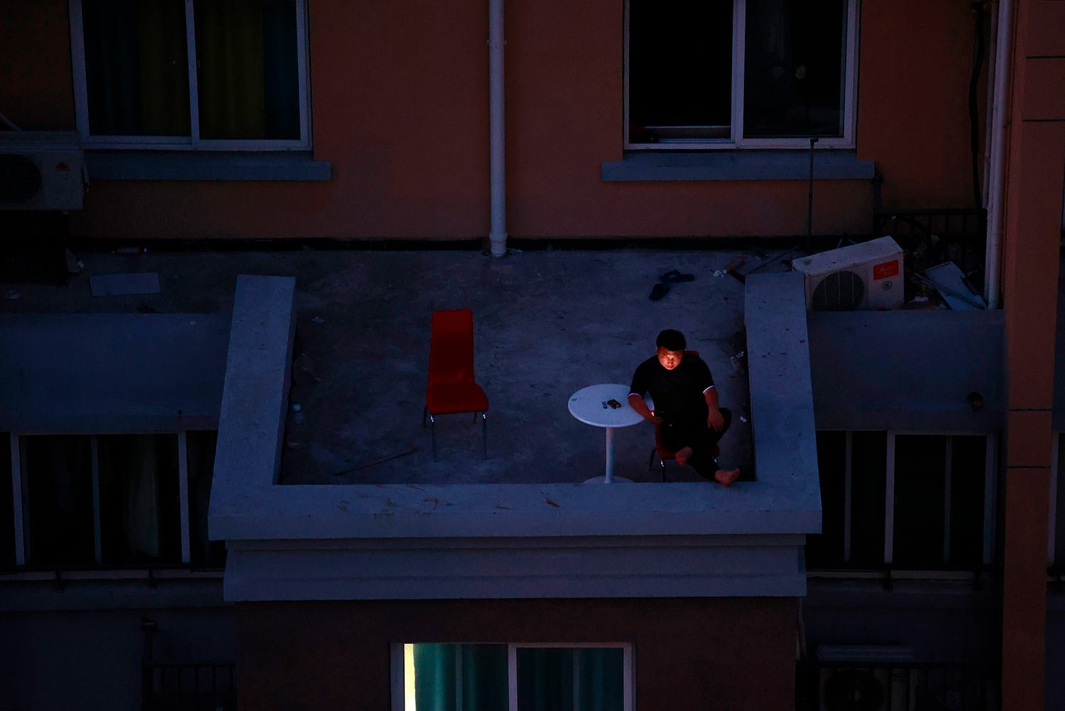  A man looks at his smartphone on a balcony in a residential community during a tight lockdown to contain a COVID-19 surge in Shanghai, China, Monday, April 11 2022.  (AP Photo) 