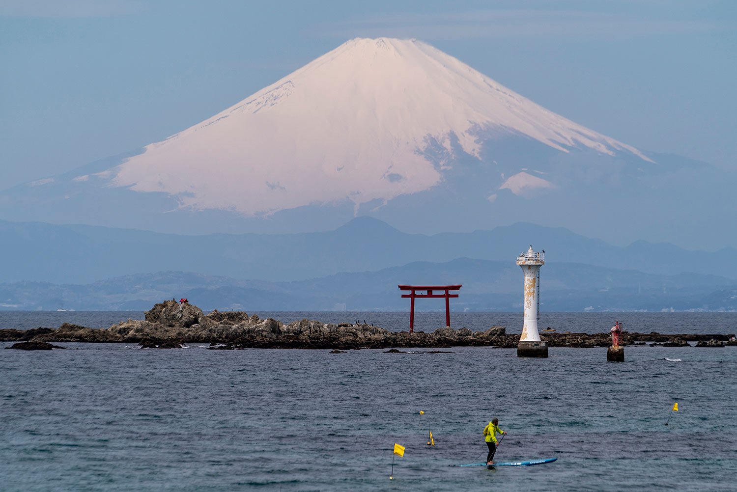  With Mount Fuji in the background, a standup paddleboarder cruises near a Torii gate, an entrance gate to a Shinto shrine, in Sagami Bay Wednesday, April 6, 2022, in Zushi, south of Tokyo. (AP Photo/Kiichiro Sato) 