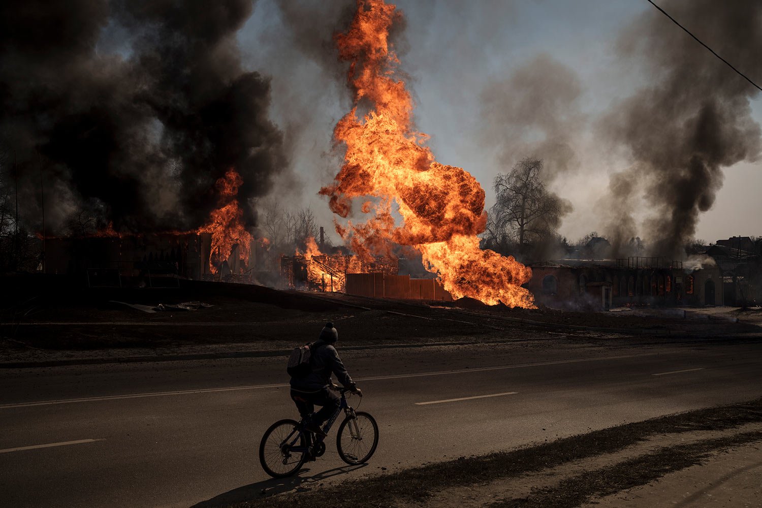  A man rides his bike past flames and smoke rising from a fire following a Russian attack in Kharkiv, Ukraine, Friday, March 25, 2022. (AP Photo/Felipe Dana)  
