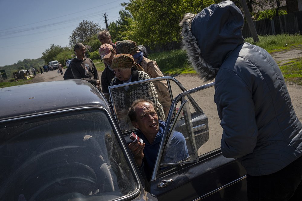 People buy cigarettes and bread from a vender in the village of Staryi Saltiv, east Kharkiv, Ukraine, Friday, May 20, 2022. The village formerly occupied by Russian forces is back under Ukrainian control, albeit very close to the front line and unde