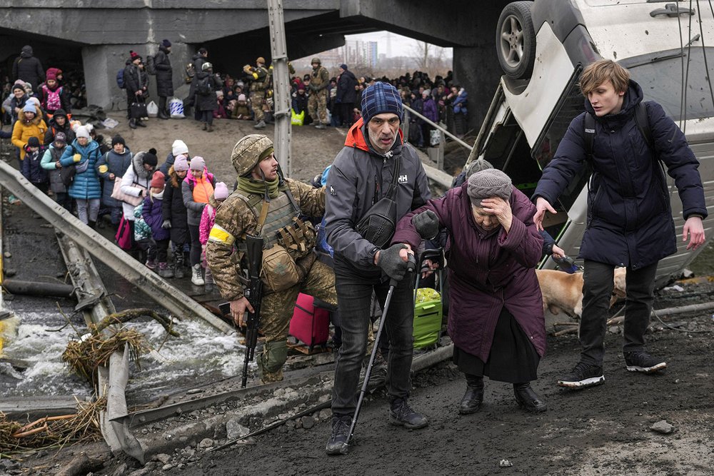  An elderly woman is assisted to cross the Irpin River on an improvised path under a bridge that was destroyed by Ukrainian troops to slow the Russian military advance while fleeing the town of Irpin, Ukraine, Saturday, March 5, 2022. (AP Photo/Vadim