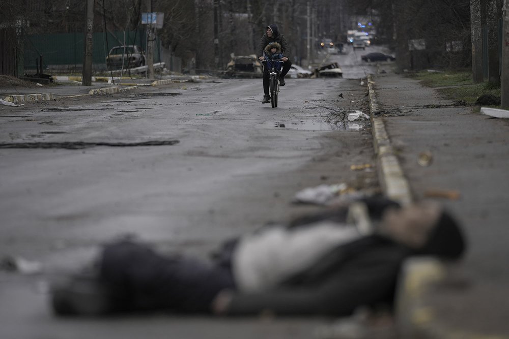  A man and child ride a bicycle through a street where civilian's bodies lie in the formerly Russian-occupied Kyiv suburb of Bucha, Ukraine, Saturday, April 2, 2022. (AP Photo/Vadim Ghirda) 