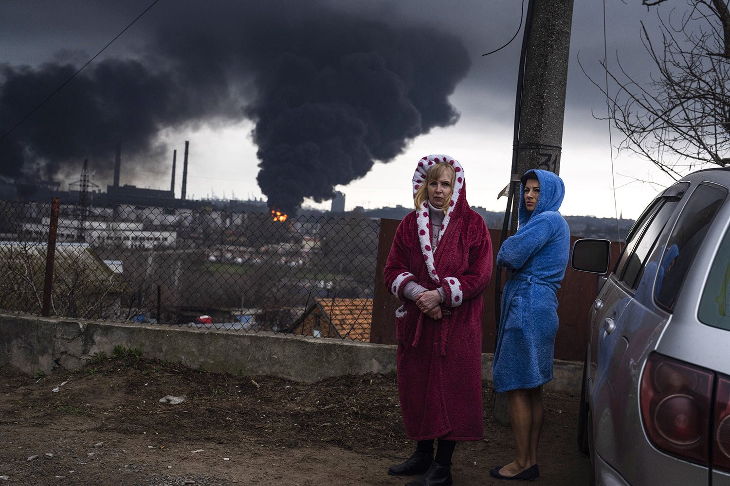  Women stand in their robes as smoke rises in the background after shelling in Odesa, Ukraine, Sunday, April 3, 2022. (AP Photo/Petros Giannakouris) 