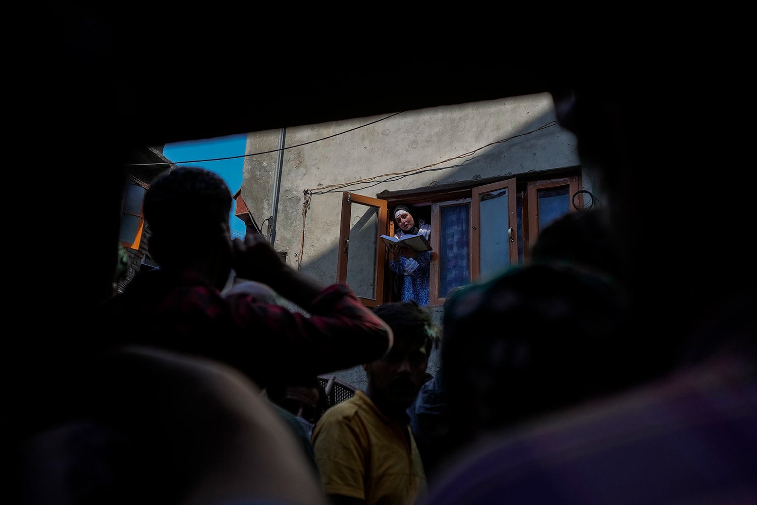  People watch as Abida Malik, sister of Kashmiri separatist leader Yasin Malik, reads verses from the Quran as she stands at the window of her house in Srinagar, Indian controlled Kashmir, Wednesday, May 25, 2022. (AP Photo/Mukhtar Khan) 